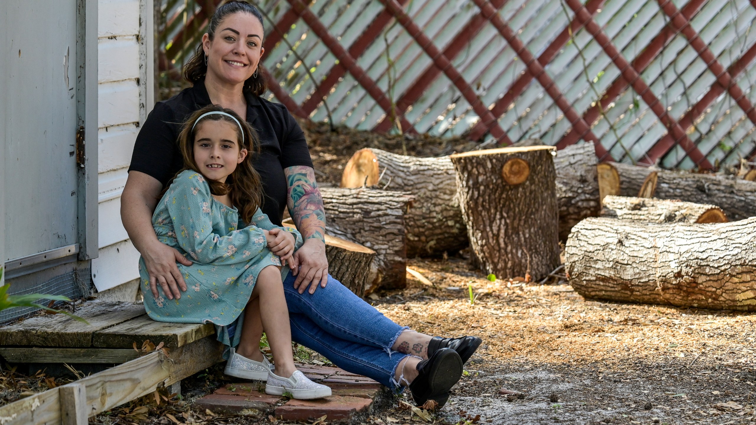 CORRECTS SPELLING OF SUBJECTS FIRST NAME TO CECILIA - Cecilia Grove and her daughter Aria Grove sit outside their home Saturday, Nov. 16, 2024, in Sarasota, Fla., next to limbs from a tree that fell durring the recent hurricanes. (AP Photo/Steve Nesius)