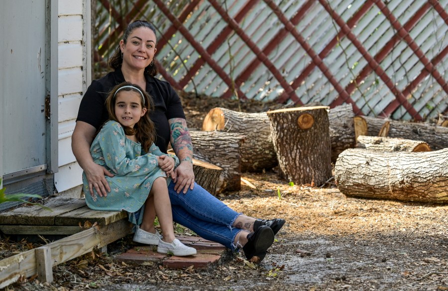 CORRECTS SPELLING OF SUBJECTS FIRST NAME TO CECILIA - Cecilia Grove and her daughter Aria Grove sit outside their home Saturday, Nov. 16, 2024, in Sarasota, Fla., next to limbs from a tree that fell durring the recent hurricanes. (AP Photo/Steve Nesius)