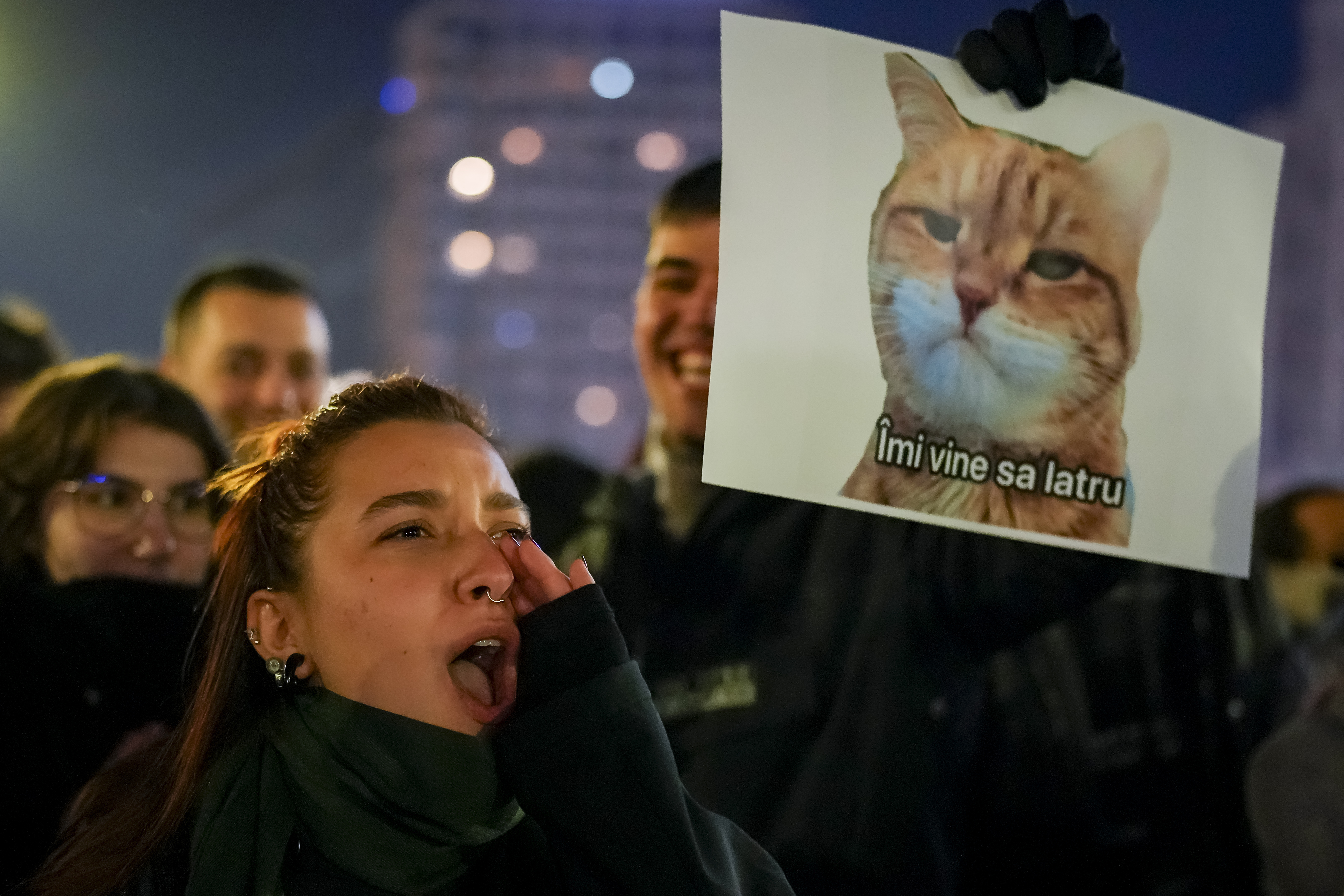 A woman shouts next to a banner depicting a grumpy cat with a text that reads "I feel like barking" in Bucharest, Romania, Wednesday, Nov. 27, 2024 during a protest against Calin Georgescu, the independent candidate for Romanian presidency who won the first round of elections making it to the Dec. 8, runoff. (AP Photo/Vadim Ghirda)