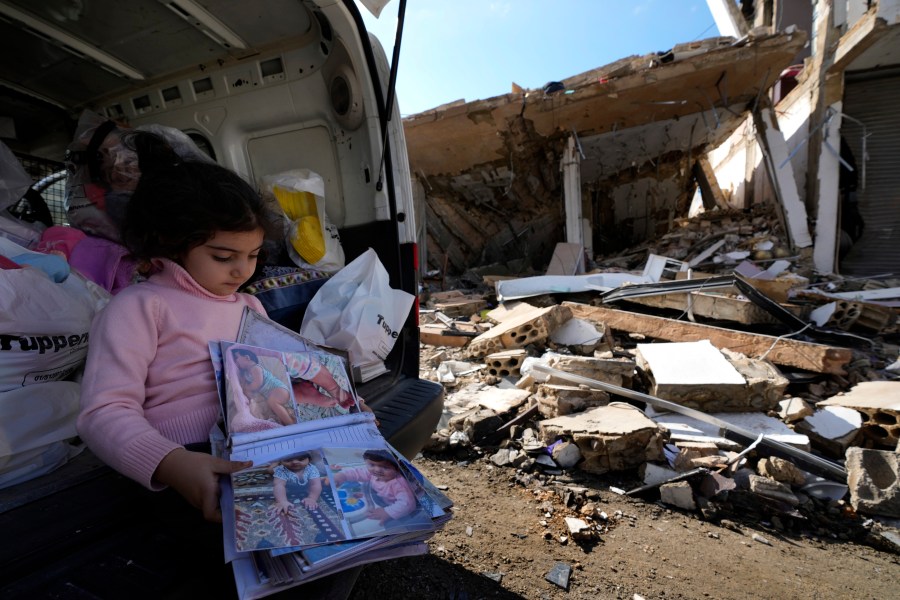 Yara Srour, 4, holds her photo album, as she sits in front of her grandparents destroyed house after she returned with her family to Hanouiyeh village, southern Lebanon, Thursday, Nov. 28, 2024 following a ceasefire between Israel and Hezbollah that went into effect on Wednesday.(AP Photo/Hussein Malla)