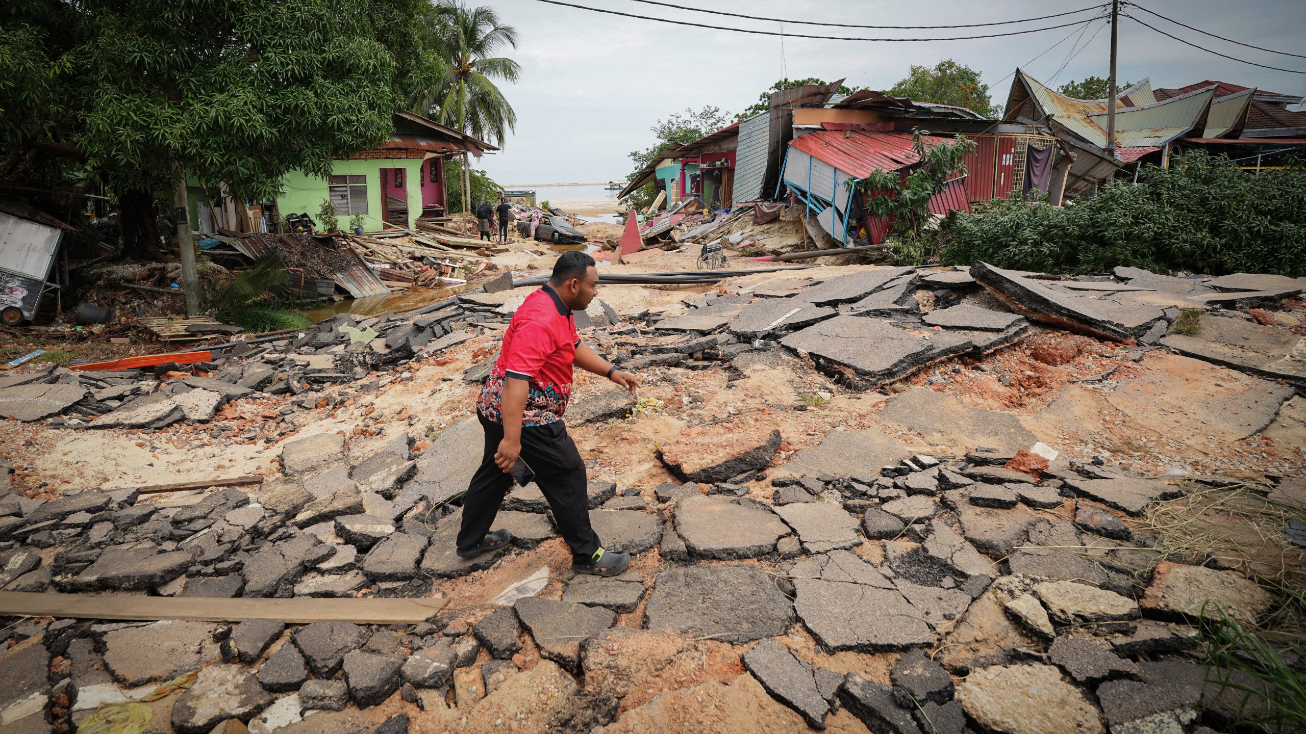 A resident crosses a road past houses damaged by flood in Tumpat, outskirts of Kota Bahru, Malaysia, Tuesday, Dec. 3, 2024. (AP Photo/Vincent Thian)