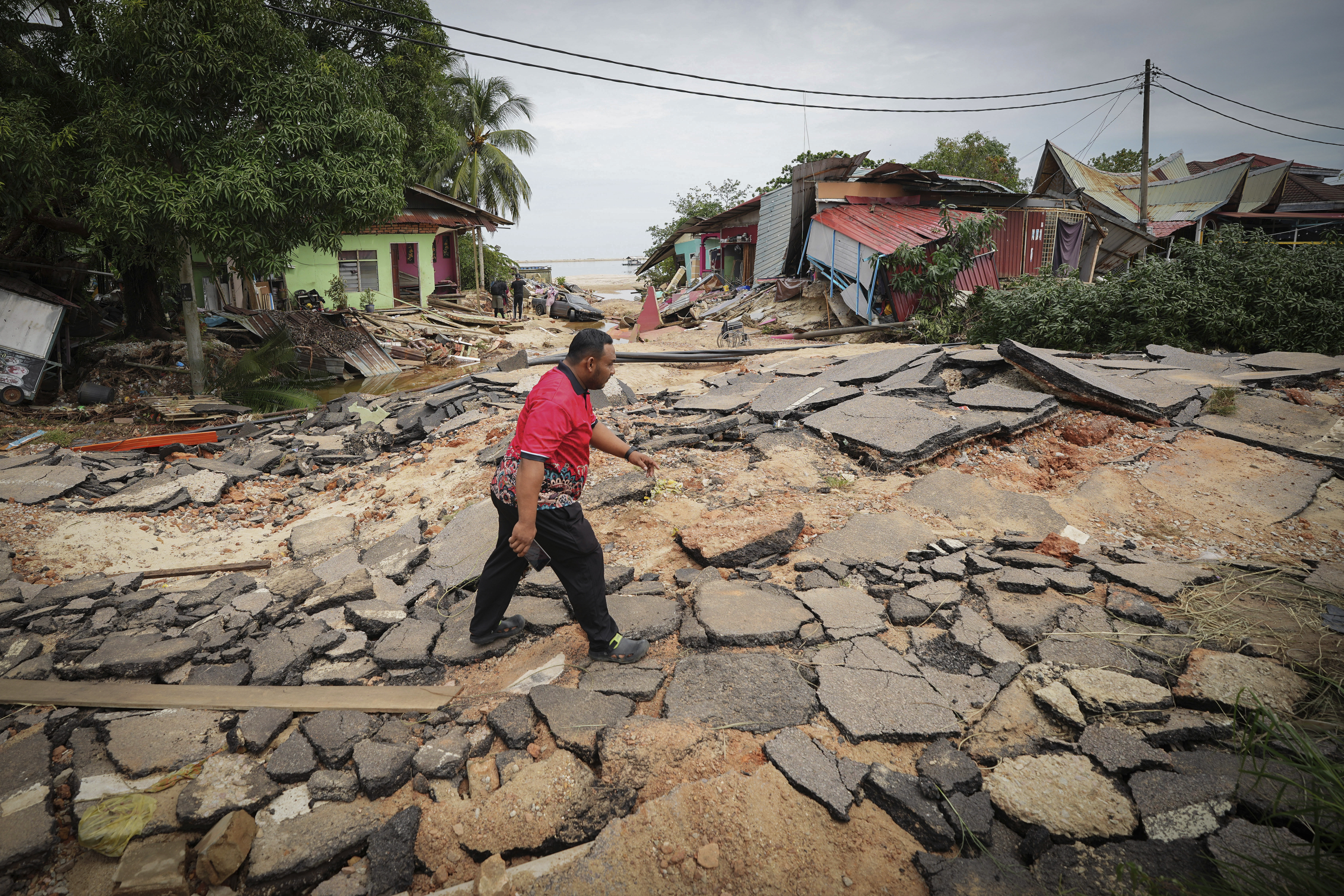 A resident crosses a road past houses damaged by flood in Tumpat, outskirts of Kota Bahru, Malaysia, Tuesday, Dec. 3, 2024. (AP Photo/Vincent Thian)