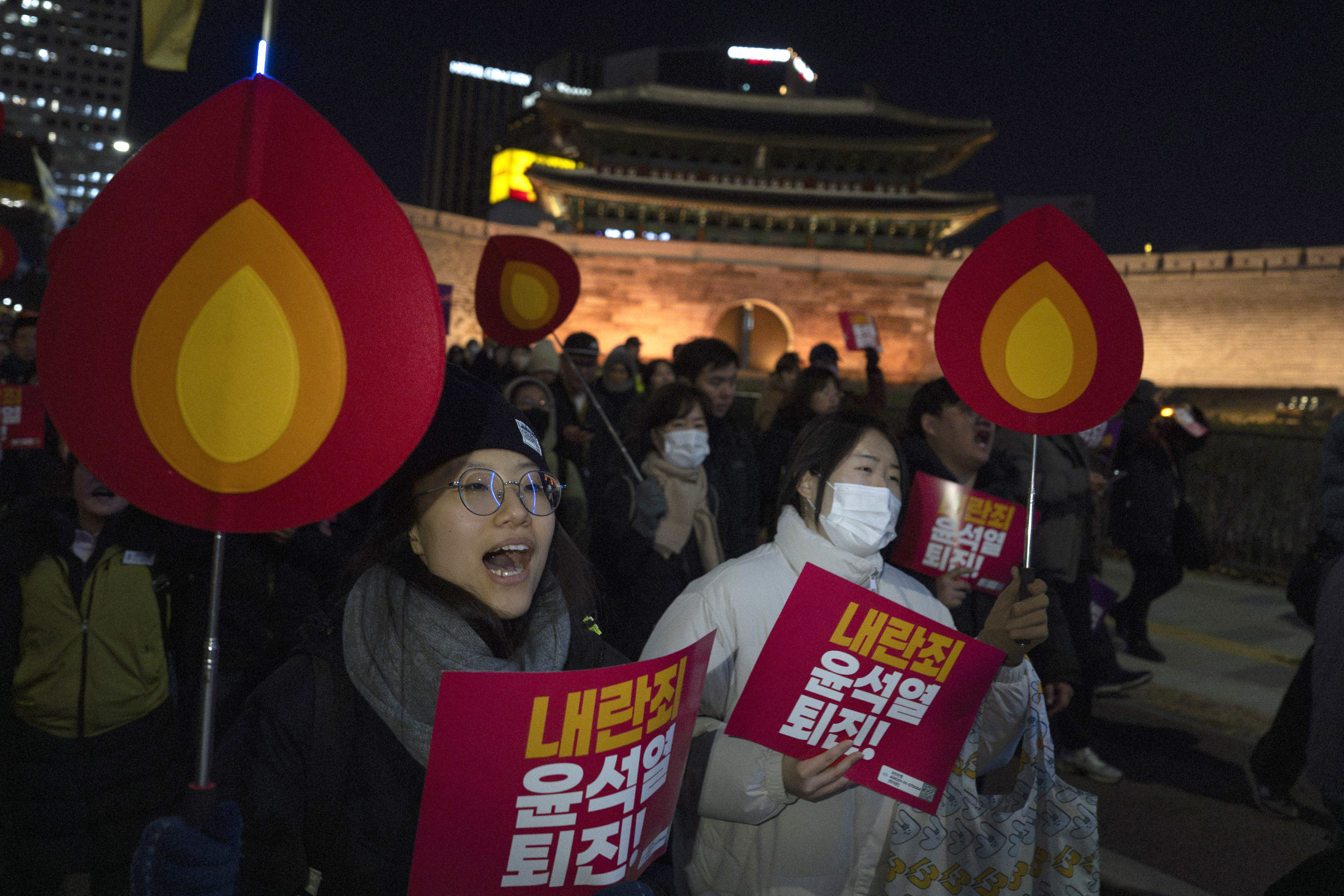 People hold signs with writing reading "Resign Yoon Suk Yeol" and shout slogans as they march to the presidential office after a candlelight vigil against South Korean President Yoon Suk Yeol, in Seoul, South Korea, Wednesday, Dec. 4, 2024 (AP Photo/Ng Han Guan)