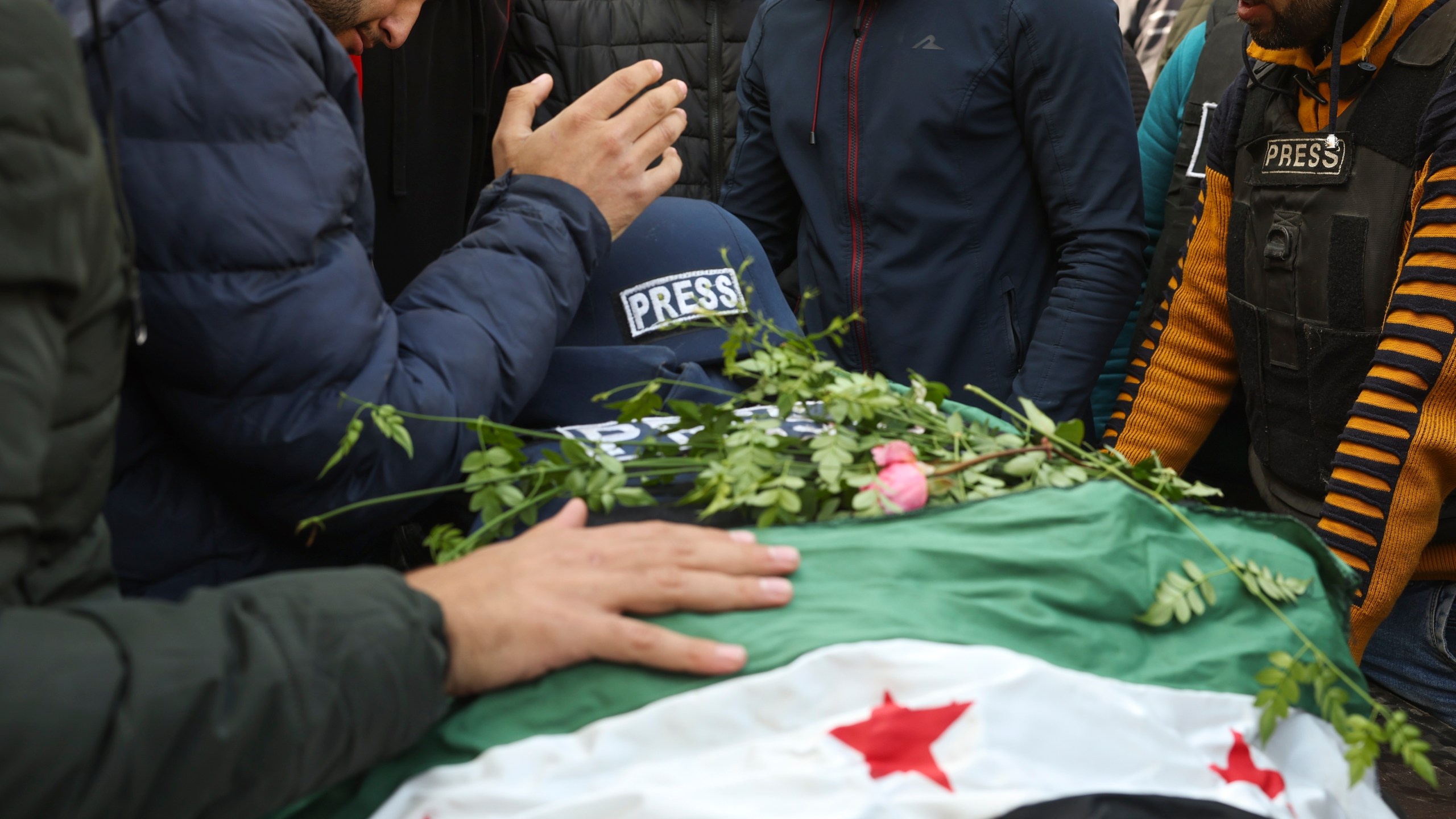 Colleagues and friends mourn over the body, covered with a Syrian opposition flag, of Syrian photographer Anas Alkharboutli, 32, in Idlib, Syria, Wednesday Dec. 4, 2024. Alkharboutli, working for the German news agency DPA was killed in an airstrike near the city of Hama, the agency said Wednesday.(AP Photo/Ghaith Alsayed)