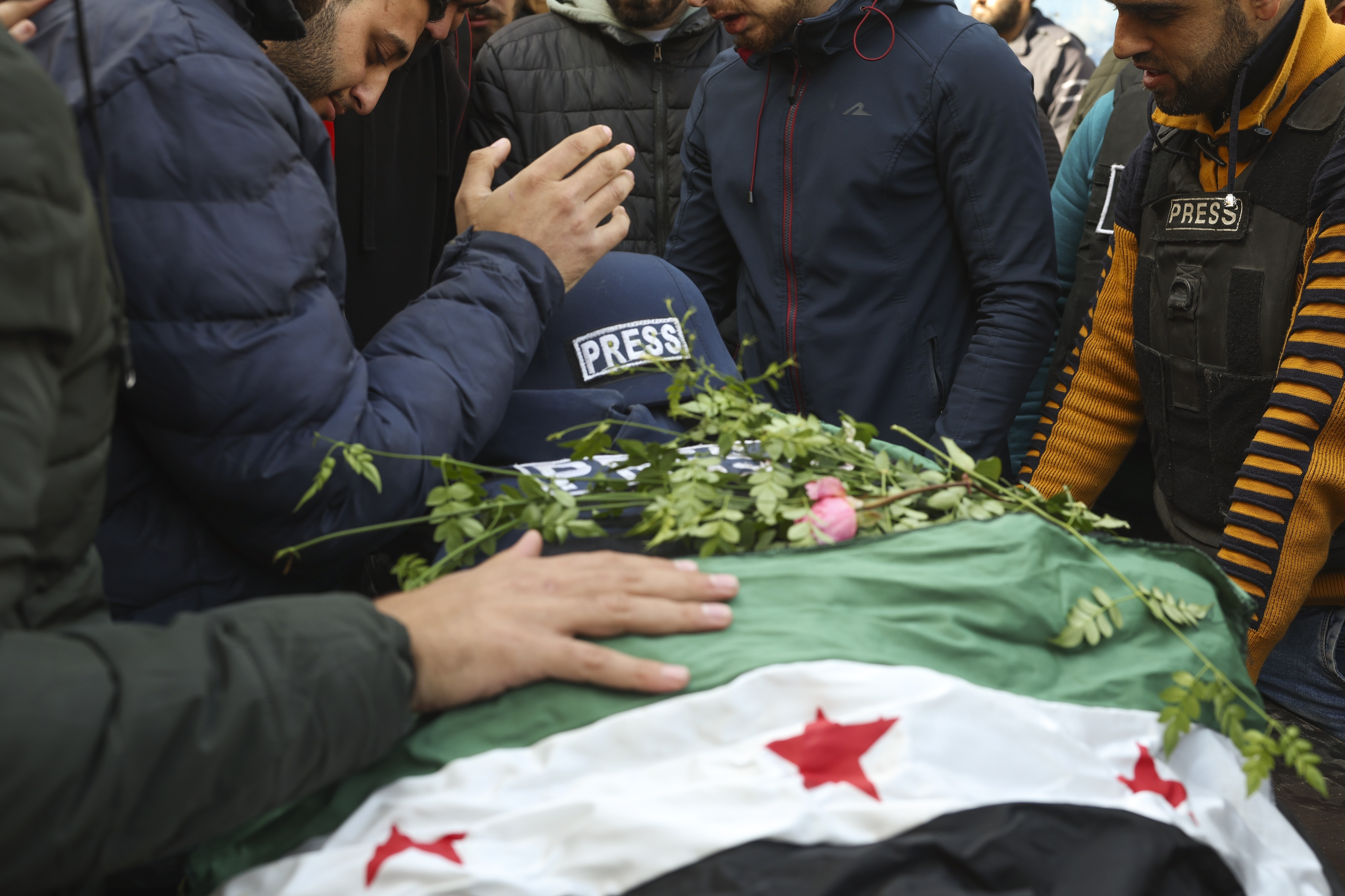 Colleagues and friends mourn over the body, covered with a Syrian opposition flag, of Syrian photographer Anas Alkharboutli, 32, in Idlib, Syria, Wednesday Dec. 4, 2024. Alkharboutli, working for the German news agency DPA was killed in an airstrike near the city of Hama, the agency said Wednesday.(AP Photo/Ghaith Alsayed)