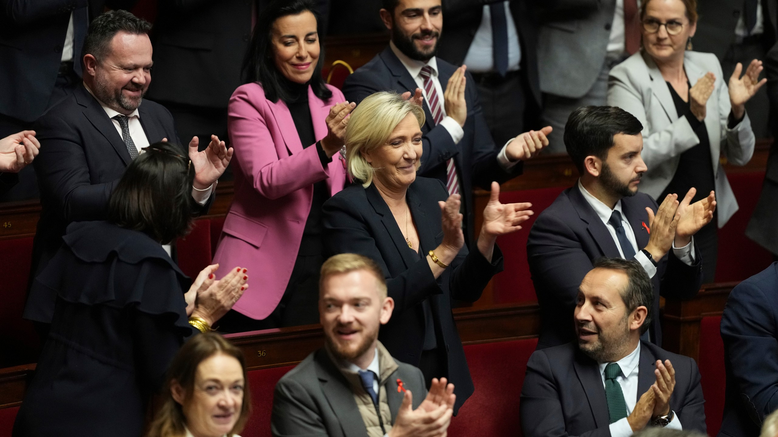 French far-right leader Marine Le Pen, center, applauds with other National Rally parliament members during conservative lawmaker Eric Ciotti's speech prior to a vote on a no-confidence motion that could bring him down and his cabinet for the first time since 1962, Wednesday, Dec. 4, 2024 the National Assembly in Paris. (AP Photo/Michel Euler)