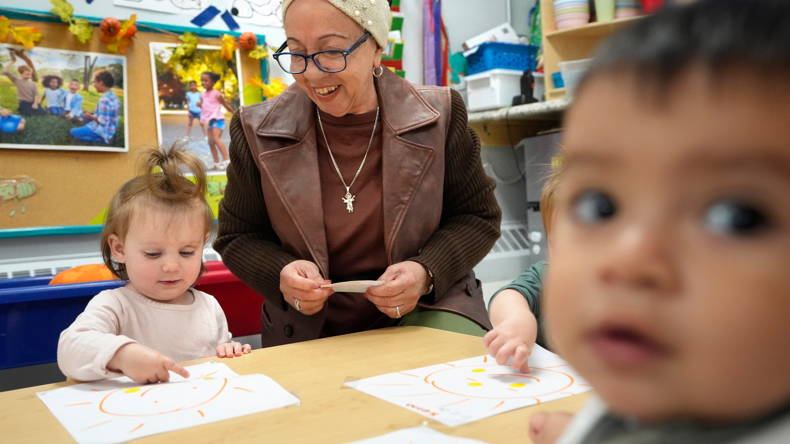 Volunteer Victoria Vasquez, 70, of Providence, R.I., center, supervises one-and-a-half year olds Scarlett Thomas, left, and Liam Echevarria Gaytan, right, in an early childcare program at Federal Hill House, Tuesday, Nov. 12, 2024, in Providence, R.I. (AP Photo/Steven Senne)