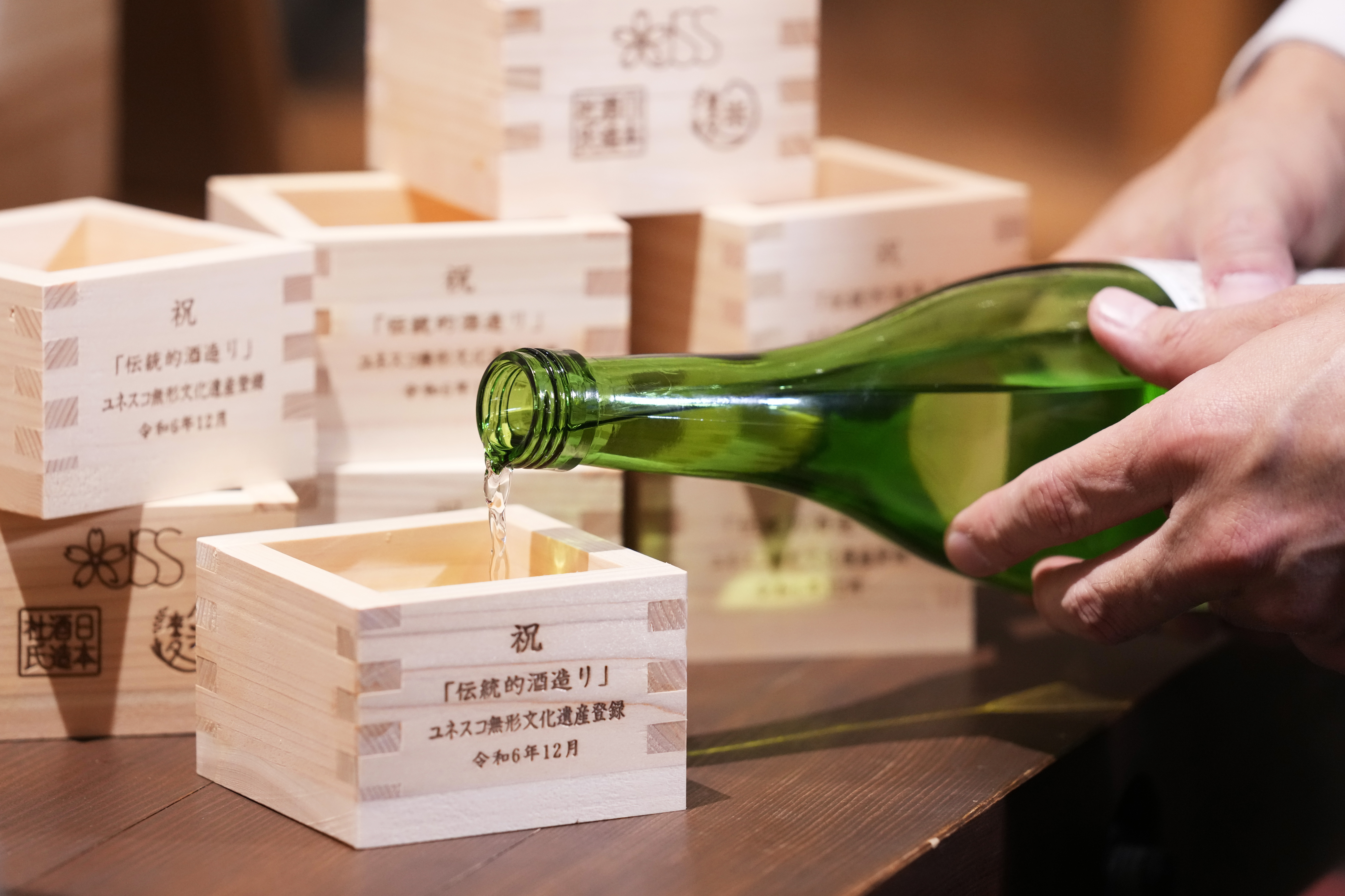 A person prepares for a display as he pours Japanese sake into a wooden cup traditionally used to drink sake, in Tokyo, Thursday, Dec. 5, 2024, before a news conference on UNESCO's recognition of Japan's sake making as "intangible cultural heritage of humanity," announced in Paraguay. (AP Photo/Hiro Komae)