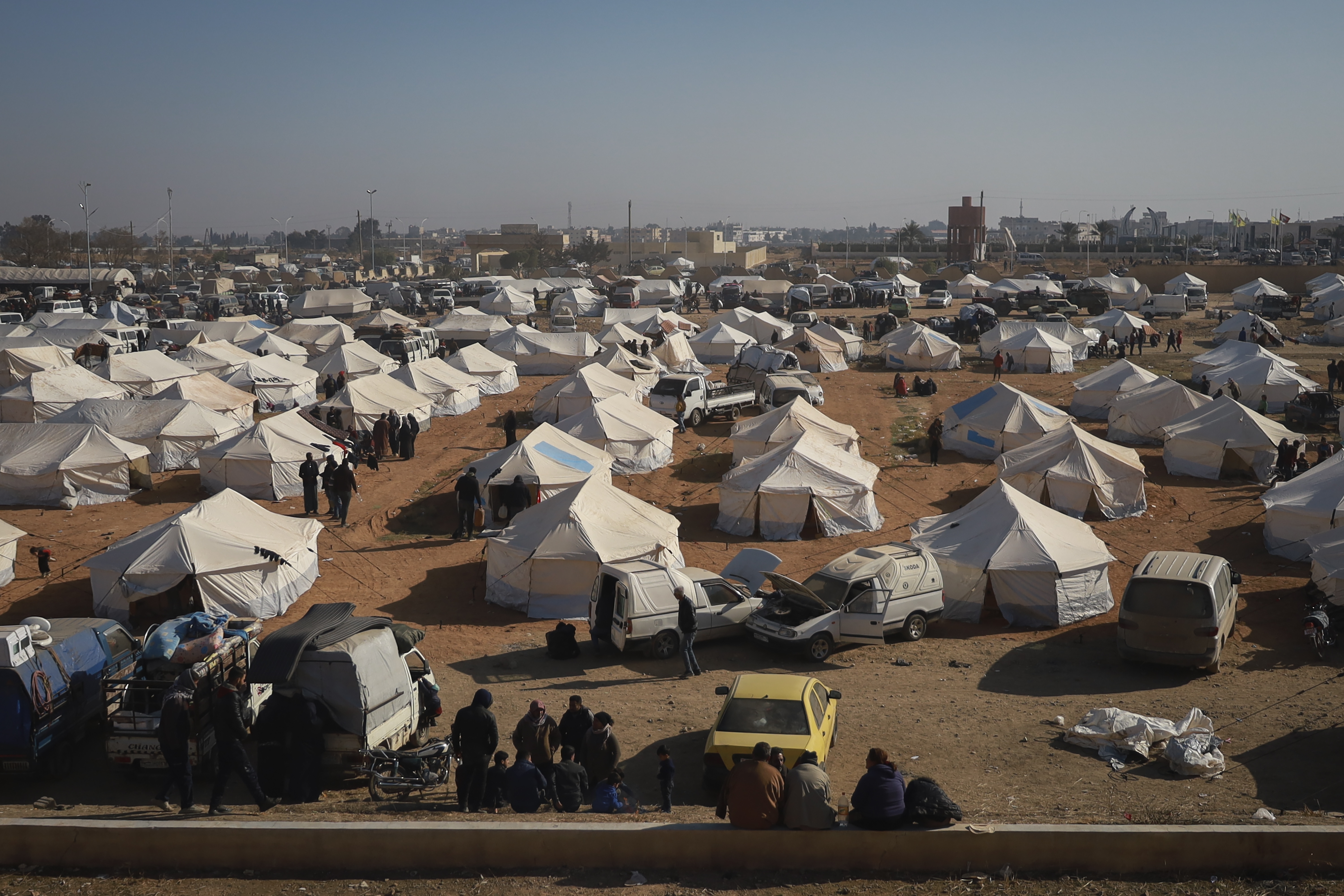 Internally displaced people walk among the tents in a camp in Tabqa city, Raqqa governorate, northern Syria, on Wednesday, Dec. 4, 2024. Thousands of Kurdish families displaced from Aleppo and Tel Rifaat have ended up in temporary shelters and on the streets in Kurdish-controlled areas of Tabqa city. (AP Photo/Hogir El Abdo)