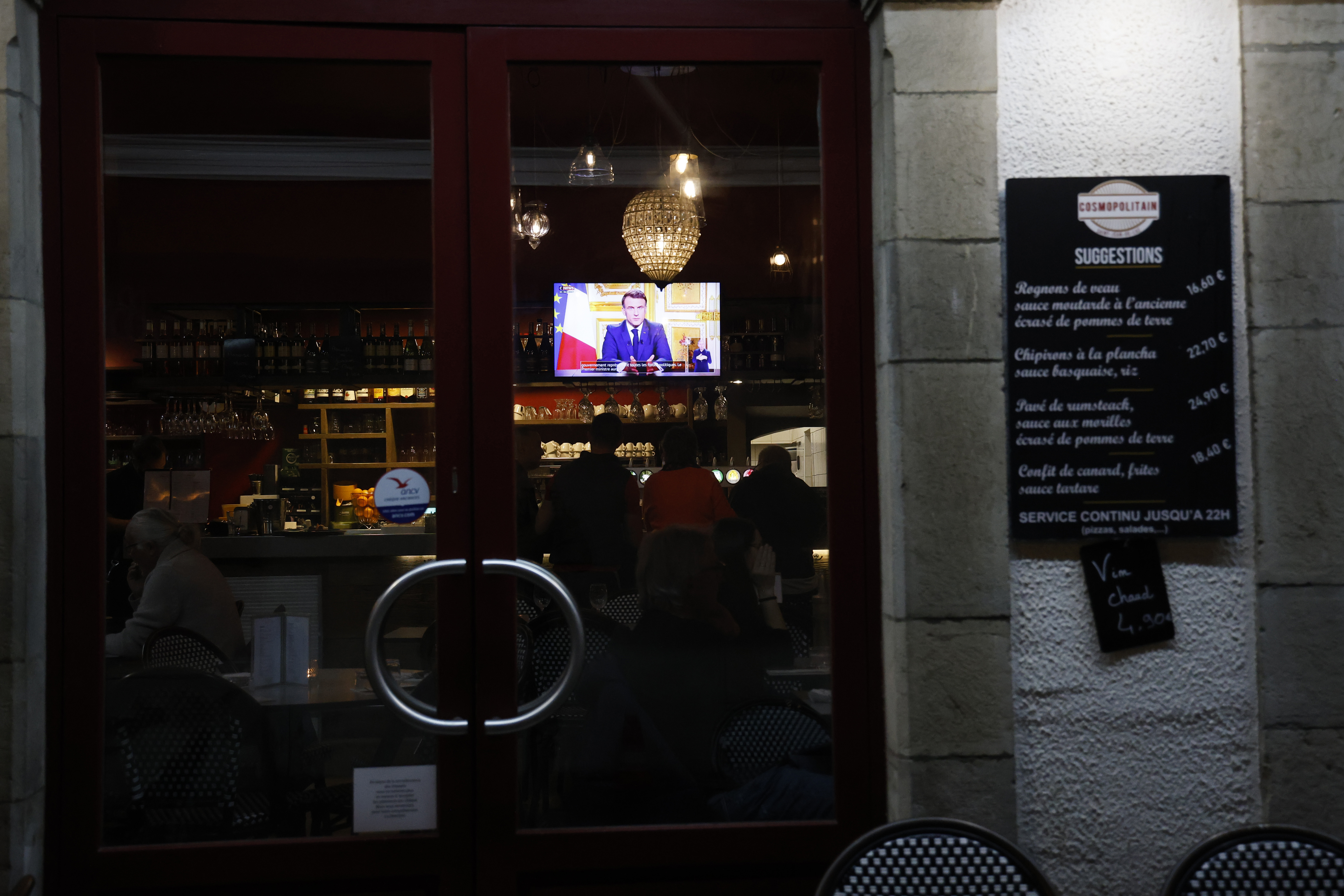 French President Emmanuel Macron addresses the nation as people enjoy a drink in a bar of Saint-Jean-de-Luz, southwestern France, Thursday, Dec. 5, 2024 (AP Photo/Nicolas Mollo)