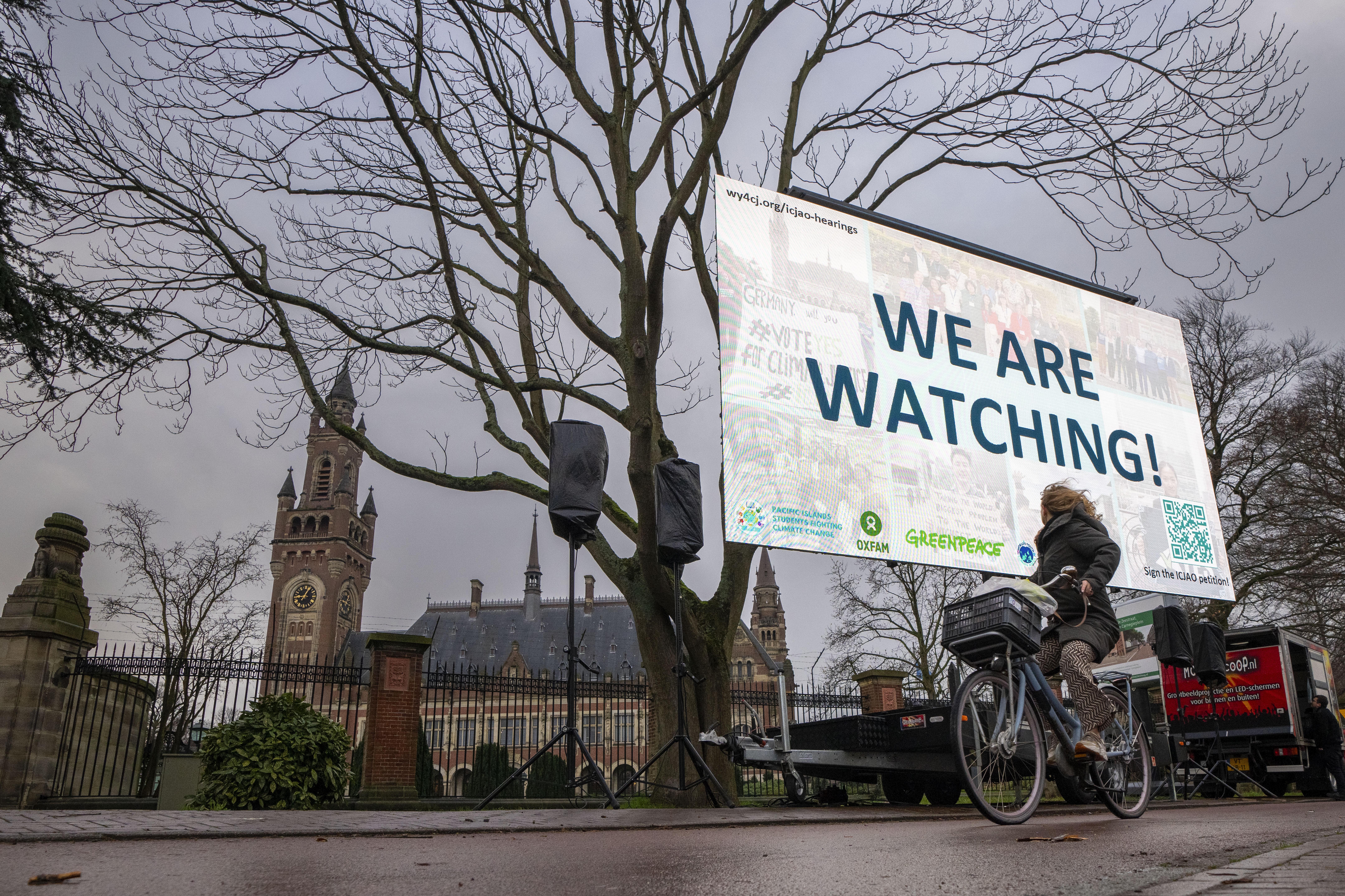 Activists protest outside the International Court of Justice, left, in The Hague, Netherlands, as it opens hearings into what countries worldwide are legally required to do to combat climate change and help vulnerable nations fight its devastating impact, Monday, Dec. 2, 2024. (AP Photo/Peter Dejong)