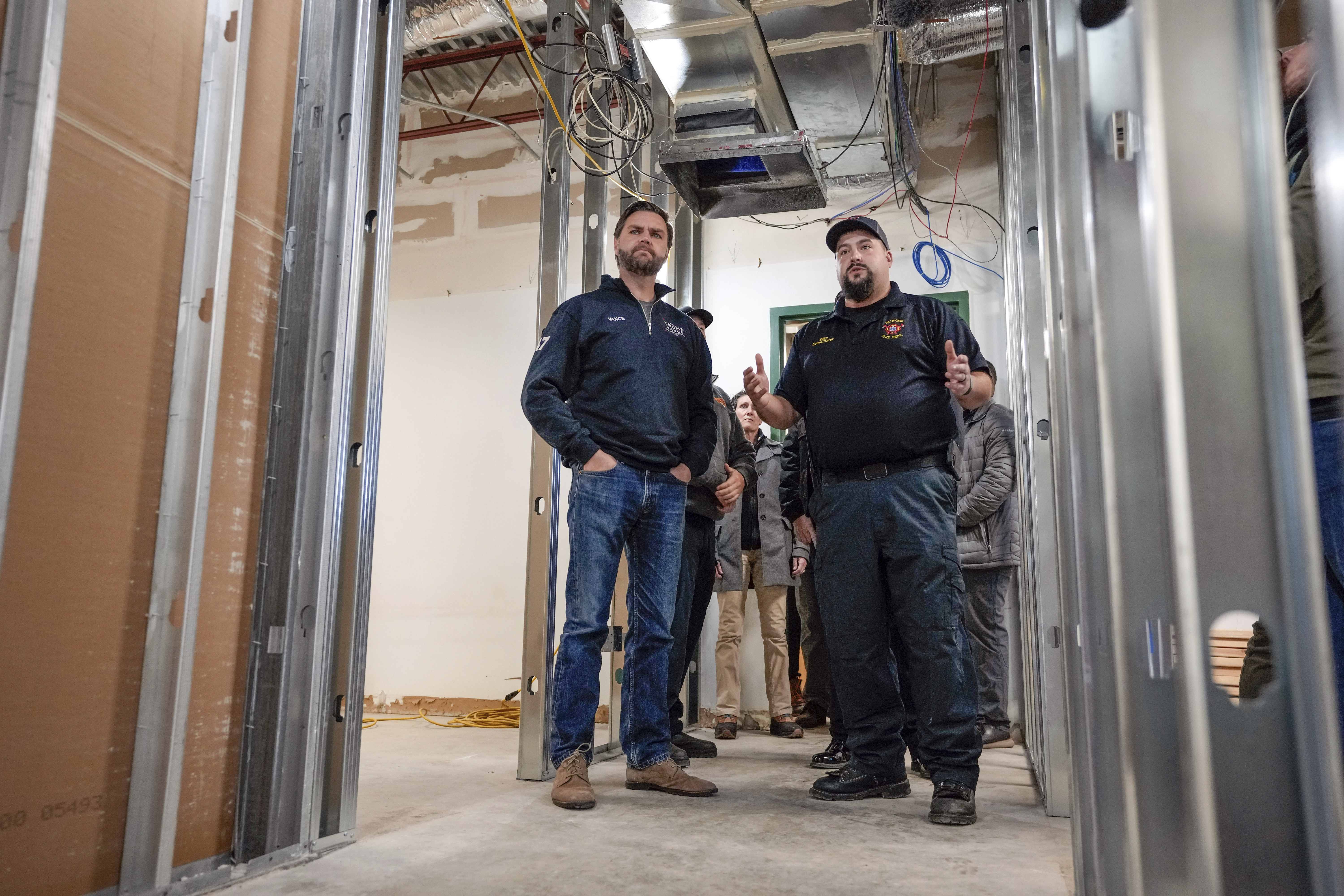 A firefighter, right, and Vice President-elect JD Vance speak during a tour of the construction of dormitories at the Fairview Volunteer Fire Department that were previously destroyed by Hurricane Helene as Vance surveys hurricane damage, Friday, Dec. 6, 2024 in Fairview, N.C. (AP Photo/Kathy Kmonicek)