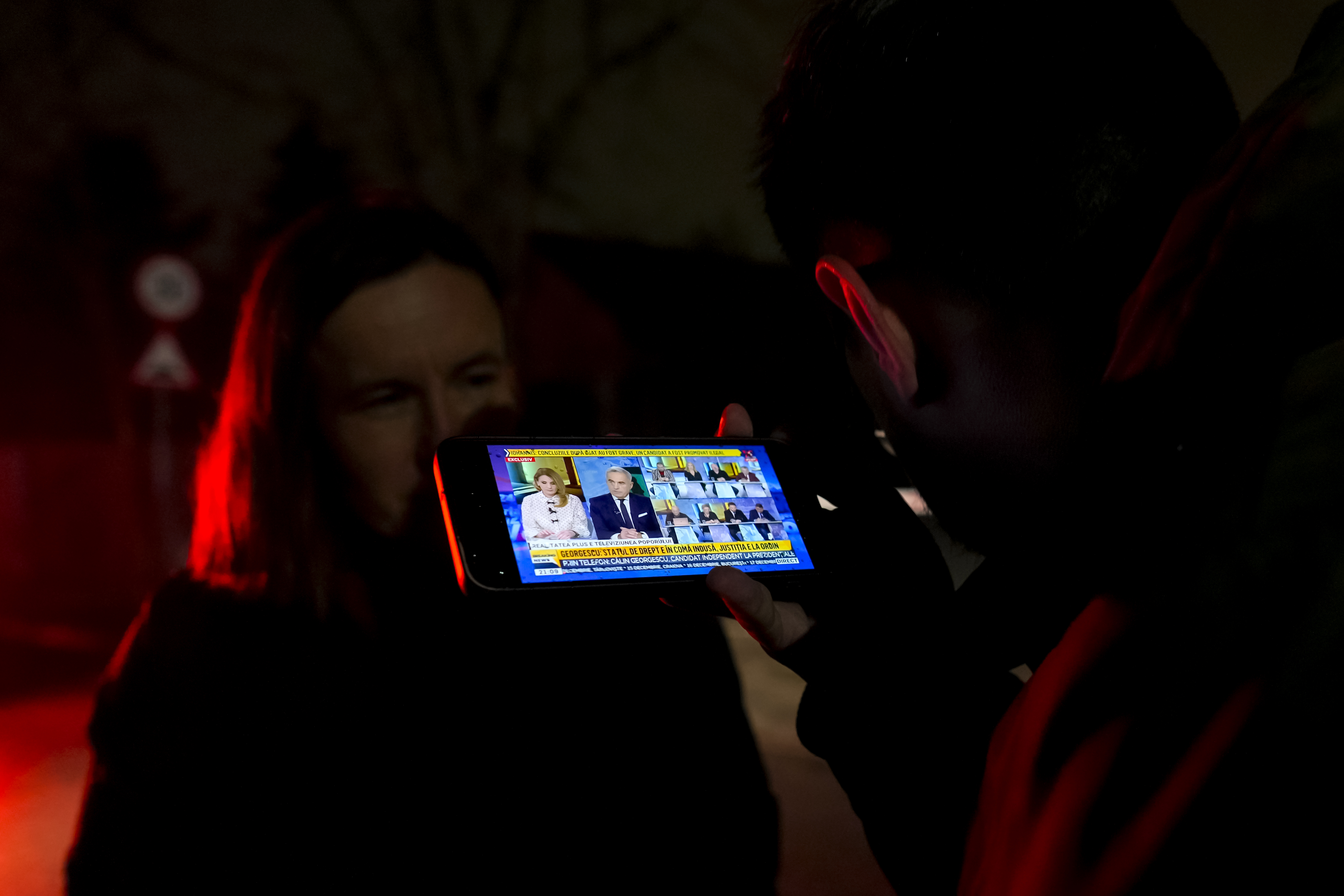 A journalist listens on his mobile phone to a live interview for a local TV channel of Calin Georgescu, the independent candidate for presidency who won the first round of presidential elections, after the Constitutional Court annulled the first round of the country's presidential election, days after allegations that Russia ran a coordinated online campaign to promote him, in Mogosoaia, Romania, Friday, Dec. 6, 2024. (AP Photo/Vadim Ghirda)