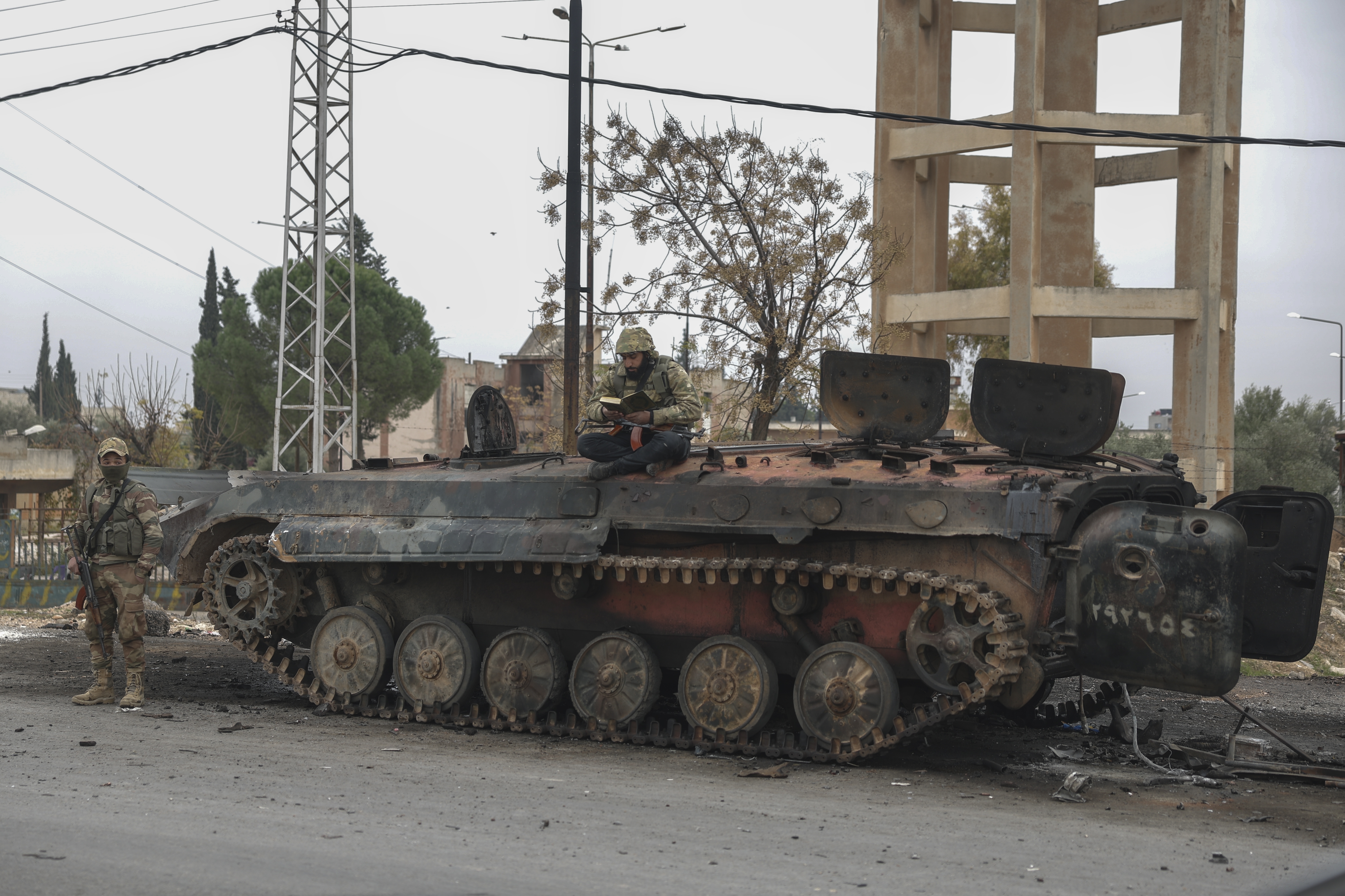 A Syrian opposition fighter reads while sitting atop a damaged government armoured vehicle near Hama, Syria, on Saturday, Dec. 7, 2024. (AP Photo/Ghaith Alsayed)