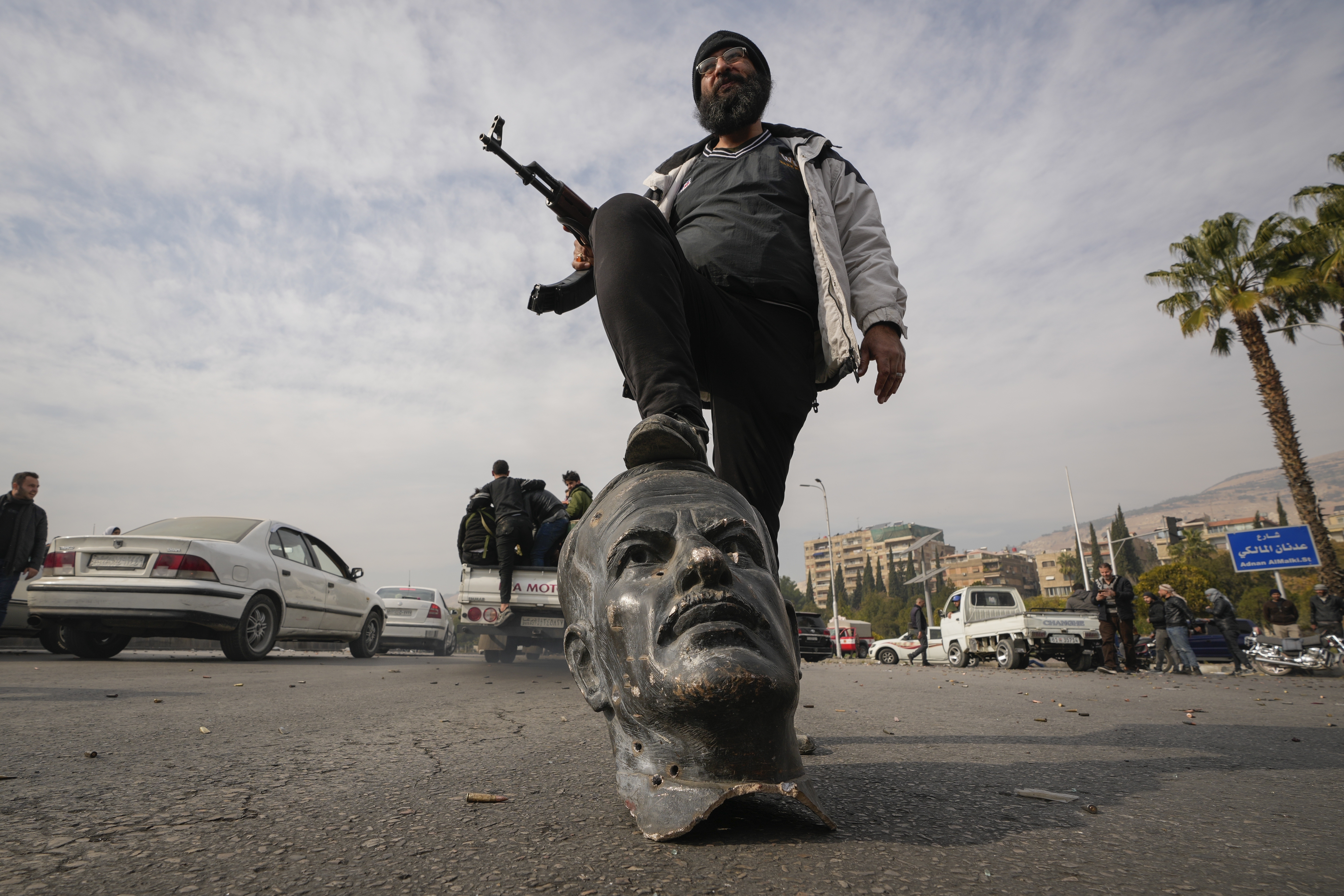 An opposition fighter steps on a broken bust of the late Syrian President Hafez Assad in Damascus, Syria, Sunday Dec. 8, 2024. (AP Photo/Hussein Malla)