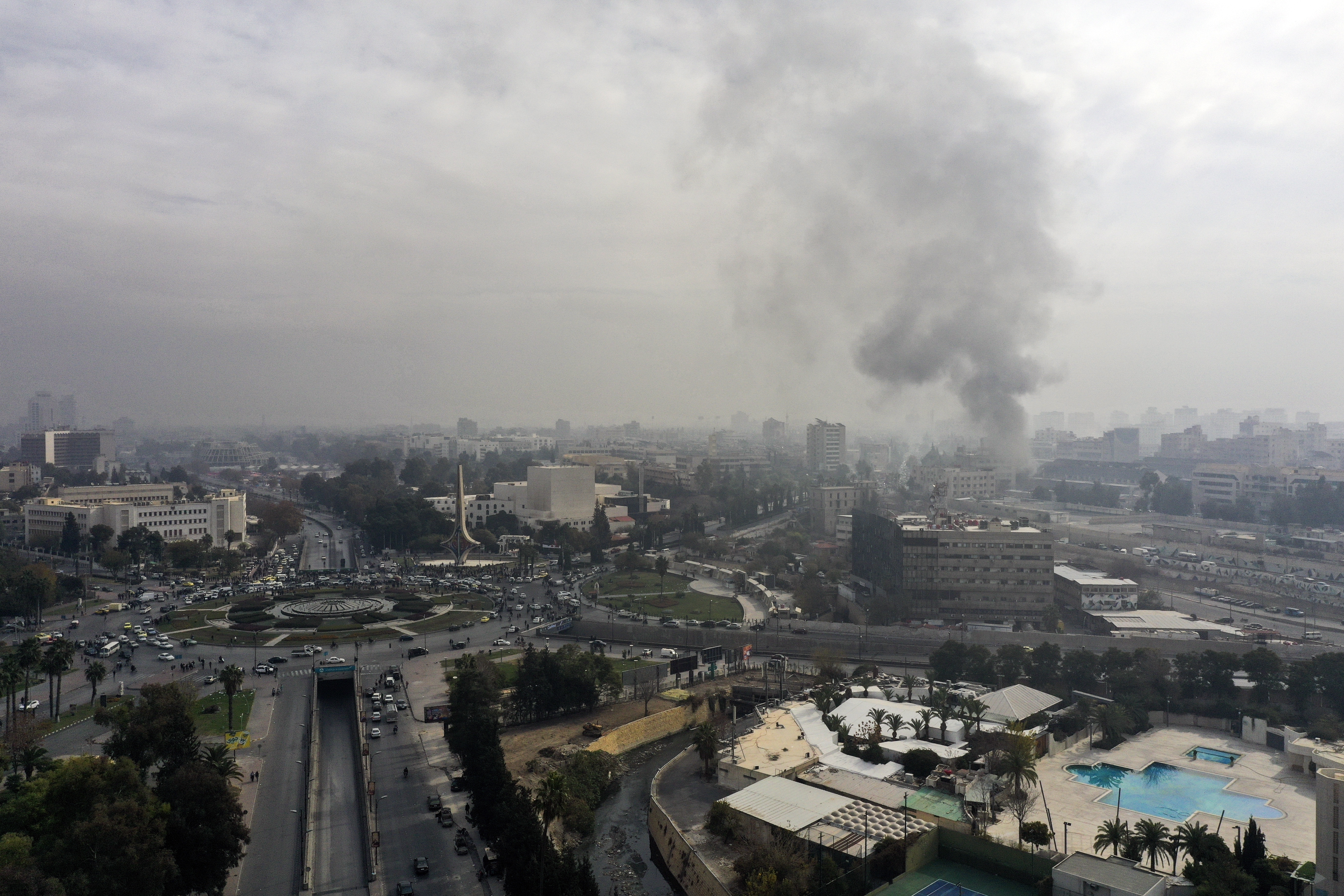 Smoke billows in the background as residents and opposition fighters celebrate in a central square after opposition forces took control of the city in Damascus, Syria, Sunday, Dec. 8, 2024. (AP Photo/Ghaith Alsayed)