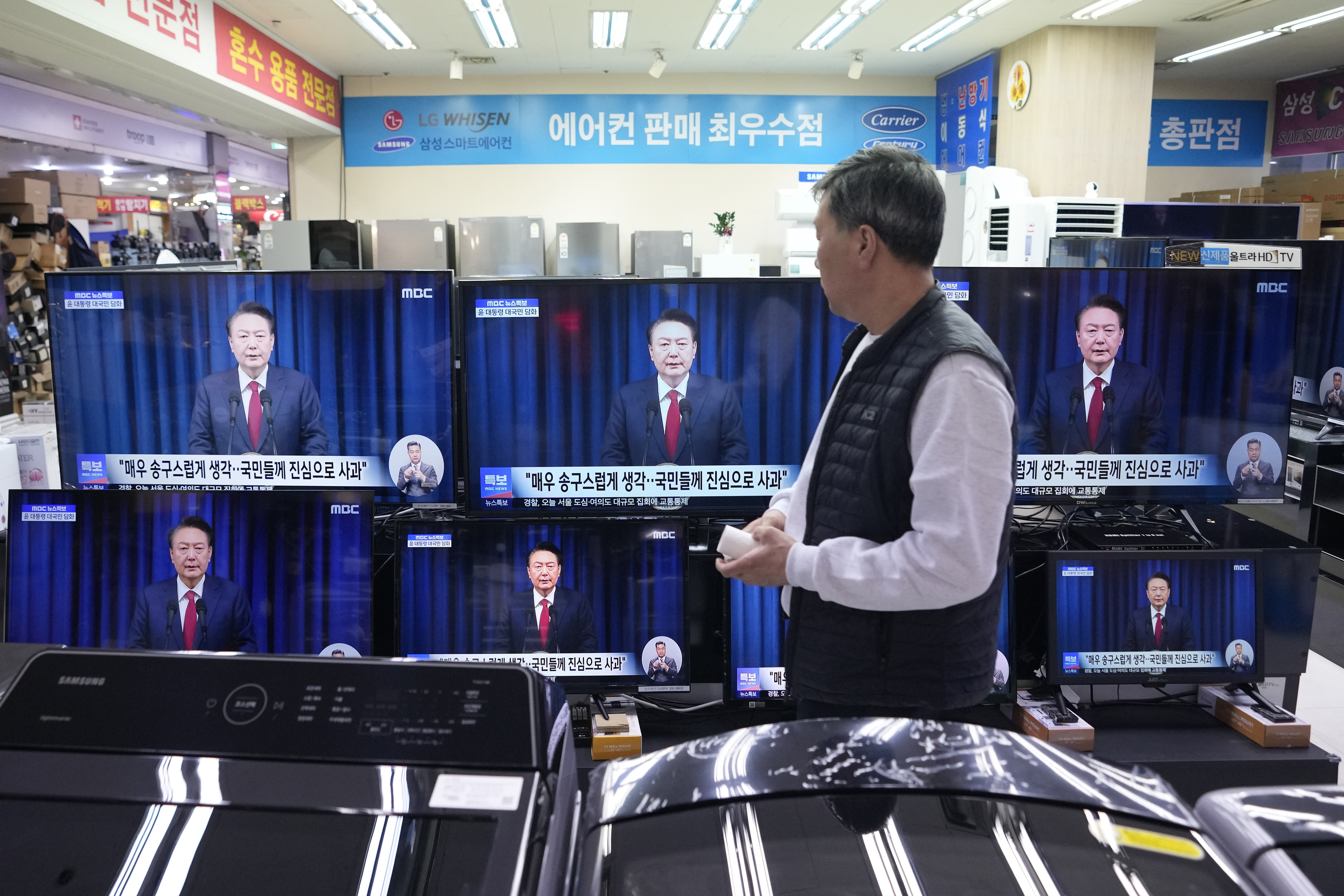 FILE - A man watches TV screens showing the broadcast of South Korean President Yoon Suk Yeol's announcement at a Yongsan Electronic store in Seoul, South Korea, Saturday, Dec. 7, 2024. (AP Photo/Ahn Young-joon, File)