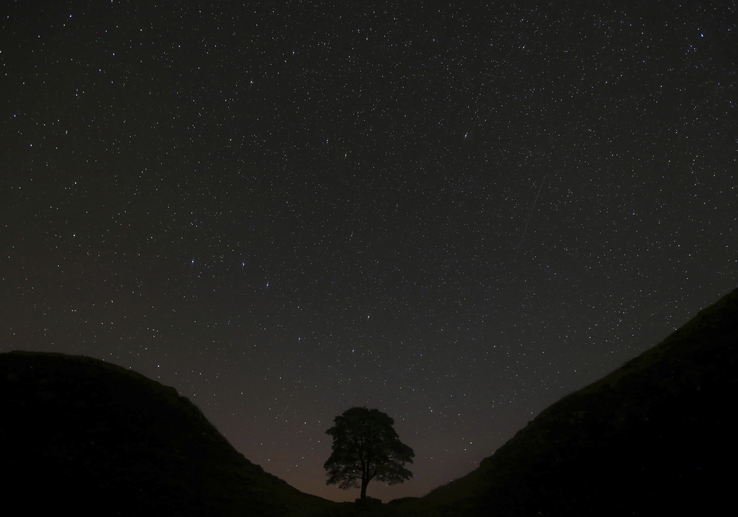 FILE - Members of the public look on at the Perseid Meteor Shower above Sycamore Gap which is along Hadrian's Wall near Bardon Mill, England, Thursday, Aug. 13, 2015. (AP Photo/Scott Heppell, File)