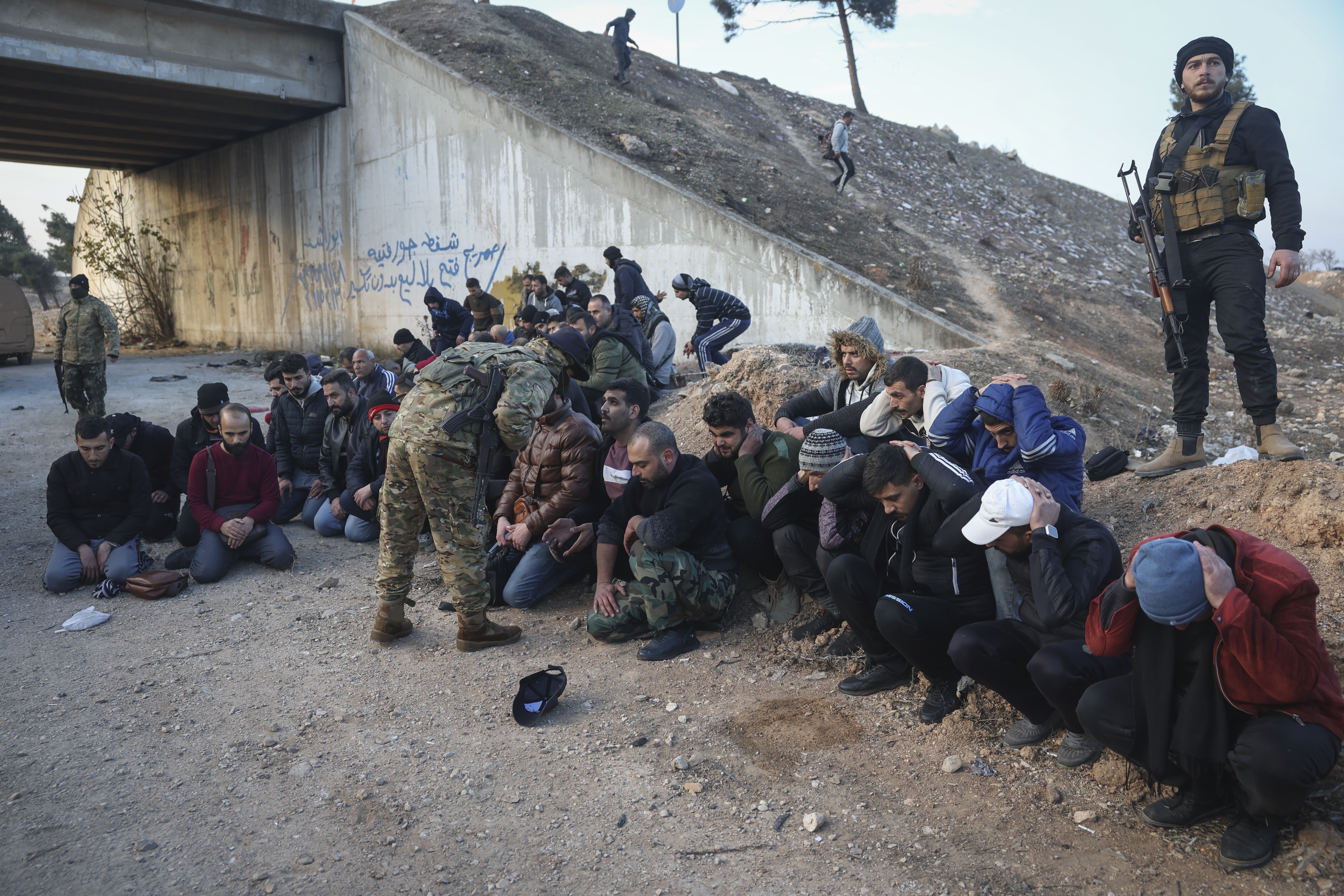 Government soldiers and allies sit on the ground as they are taken into custody by opposition fighters on the road between Homs and Damascus, near Homs, Syria, on Sunday, Dec. 8, 2024. (AP Photo/Ghaith Alsayed)