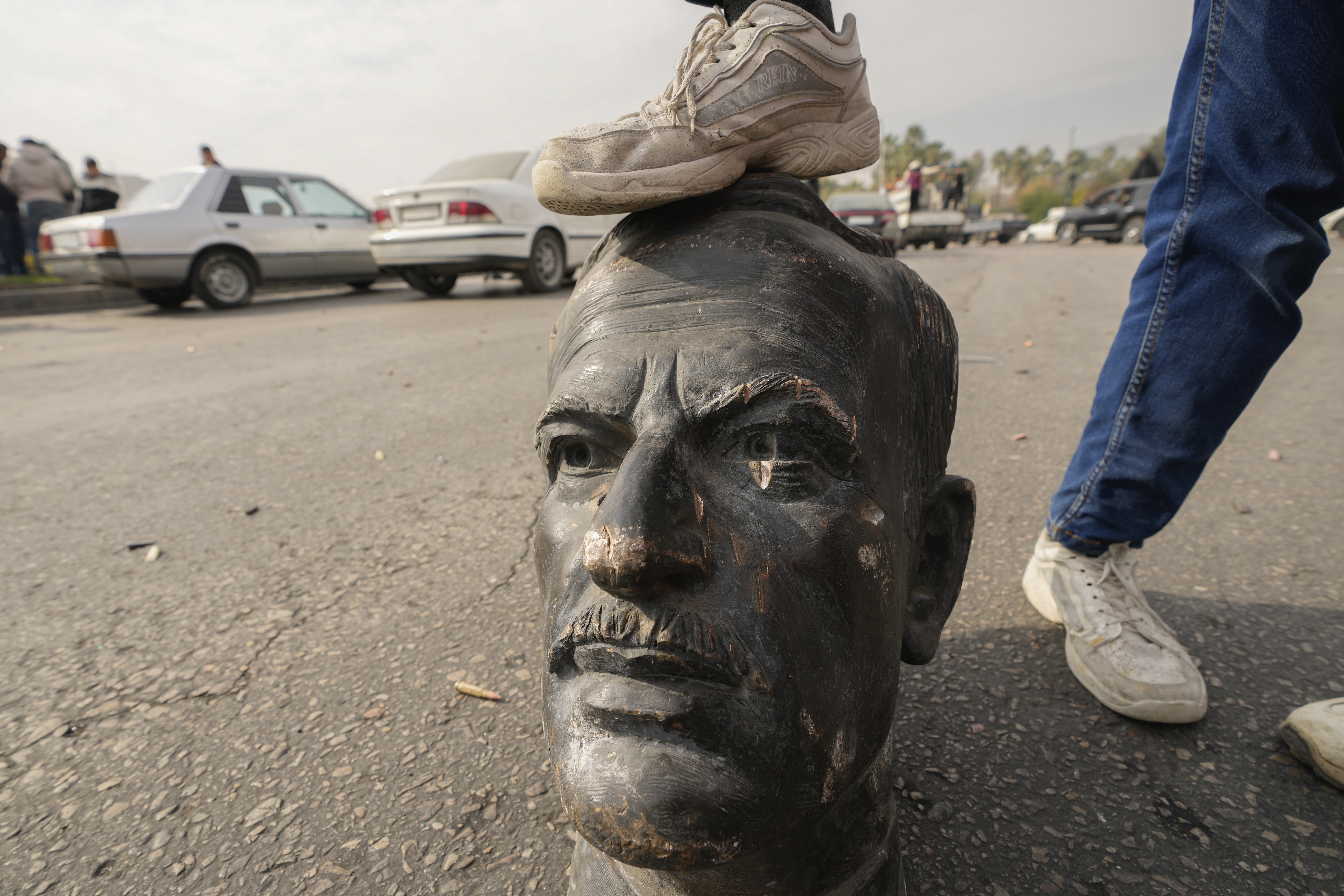 An opposition fighter steps on a broken bust of the late Syrian President Hafez Assad in Damascus, Syria, on Sunday Dec. 8, 2024. (AP Photo/Hussein Malla)