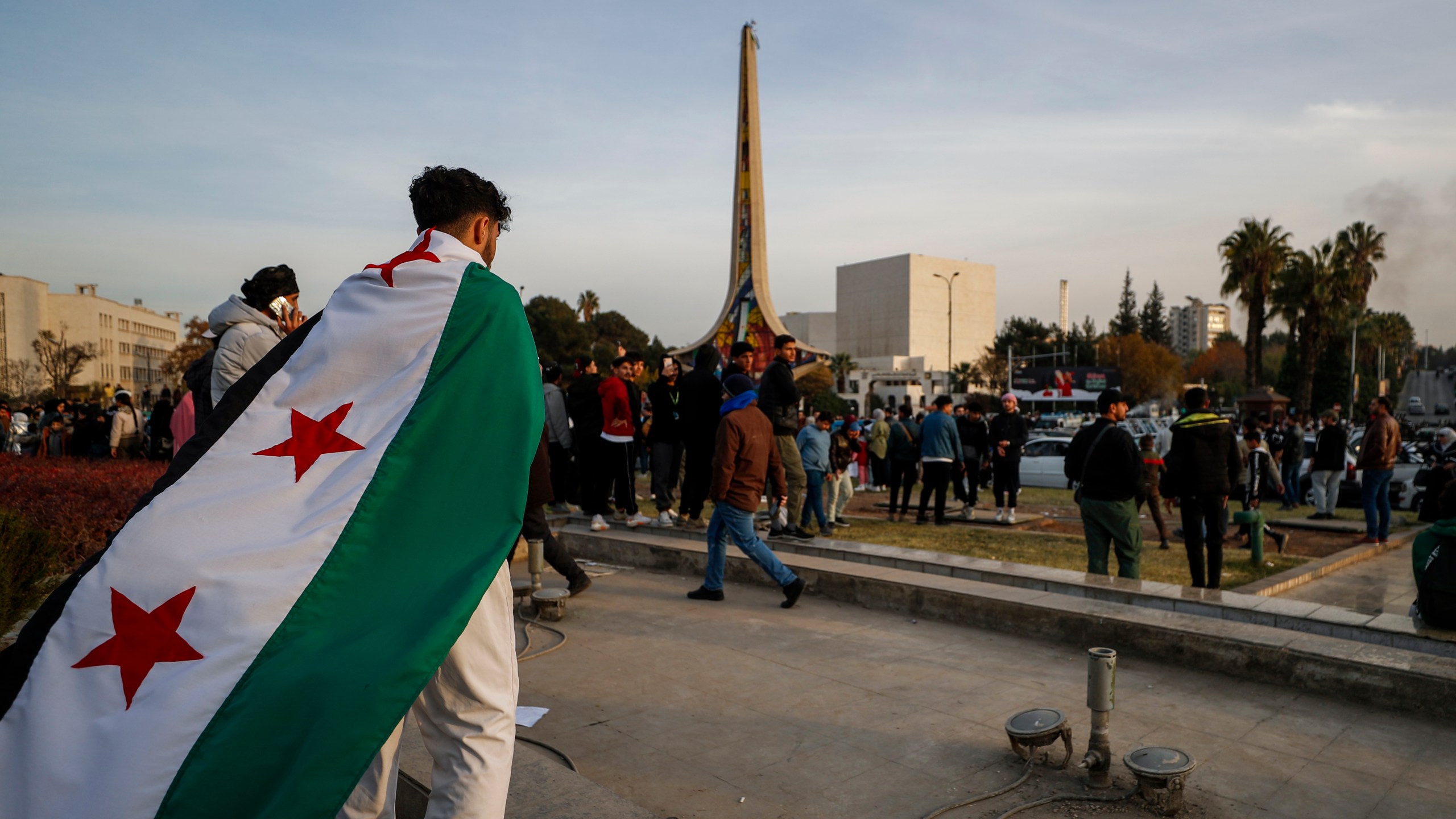 A man holds the revolutionary flag as others celebrating during the third day of the take over of the city by the insurgents in Damascus, Syria, Tuesday, Dec. 10, 2024. (AP Photo/Omar Sanadiki)