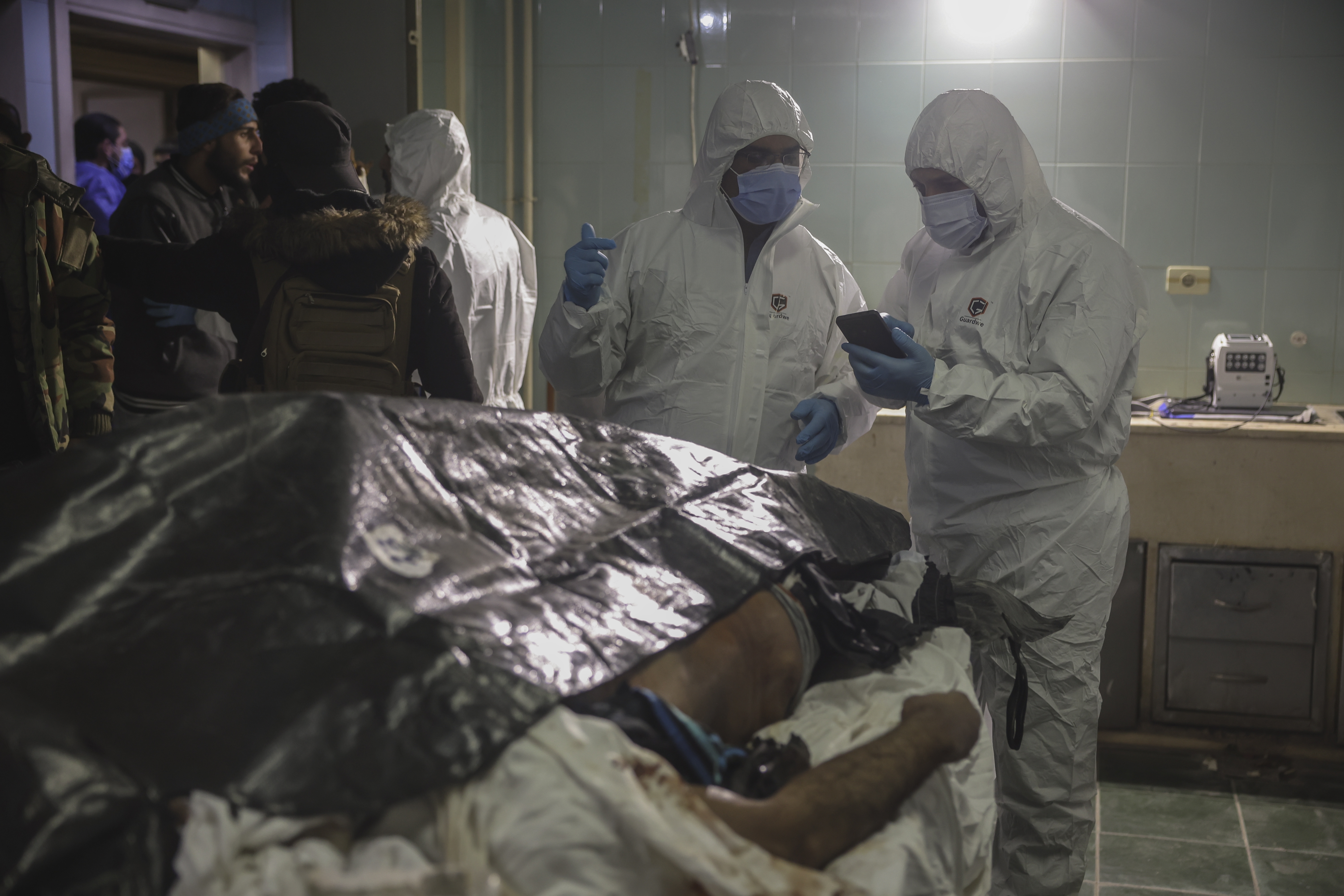 Forensic workers stand next to a body as people wait outside the morgue to identify missing relatives or friends at the Al-Mujtahid hospital in Damascus, Syria, Tuesday, Dec. 10, 2024. (AP Photo/Ghaith Alsayed)