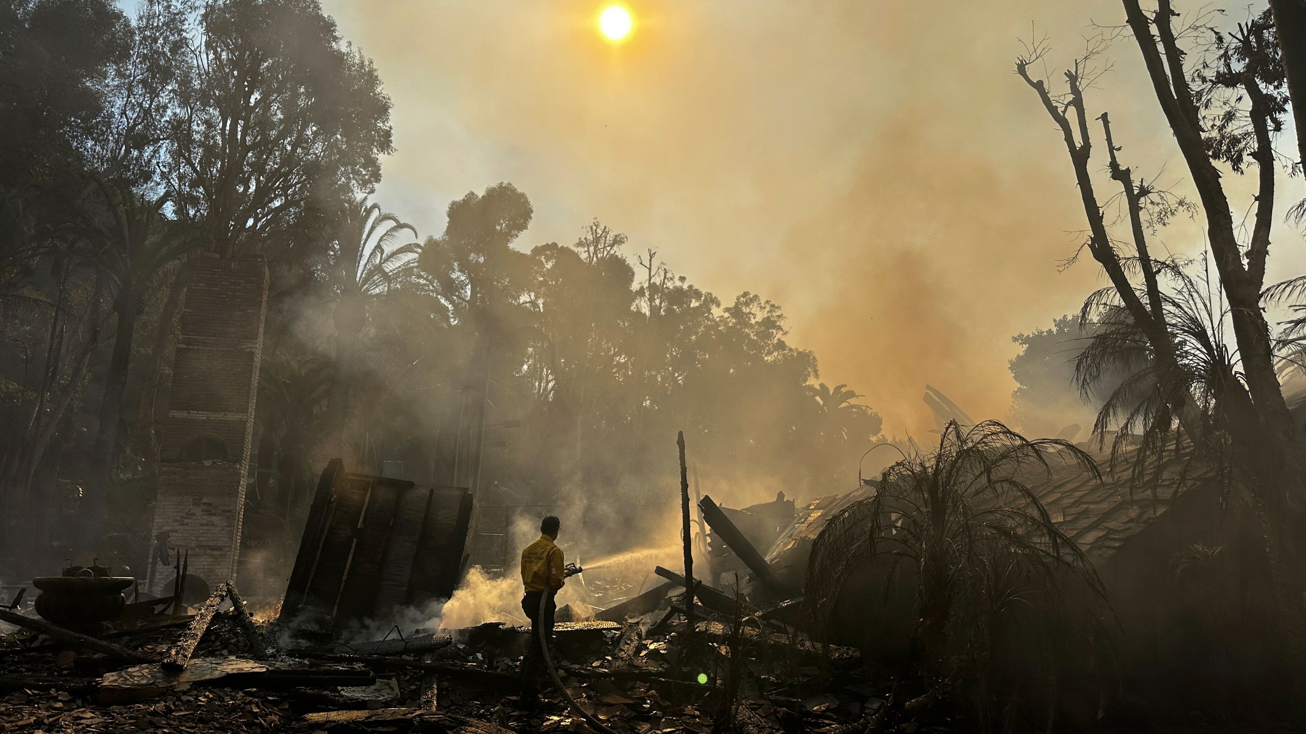 A firefighter hoses down hot spots around a fire-ravaged property after the Franklin Fire swept through Tuesday, Dec. 10, 2024, in Malibu, Calif. (AP Photo/Eugene Garcia)