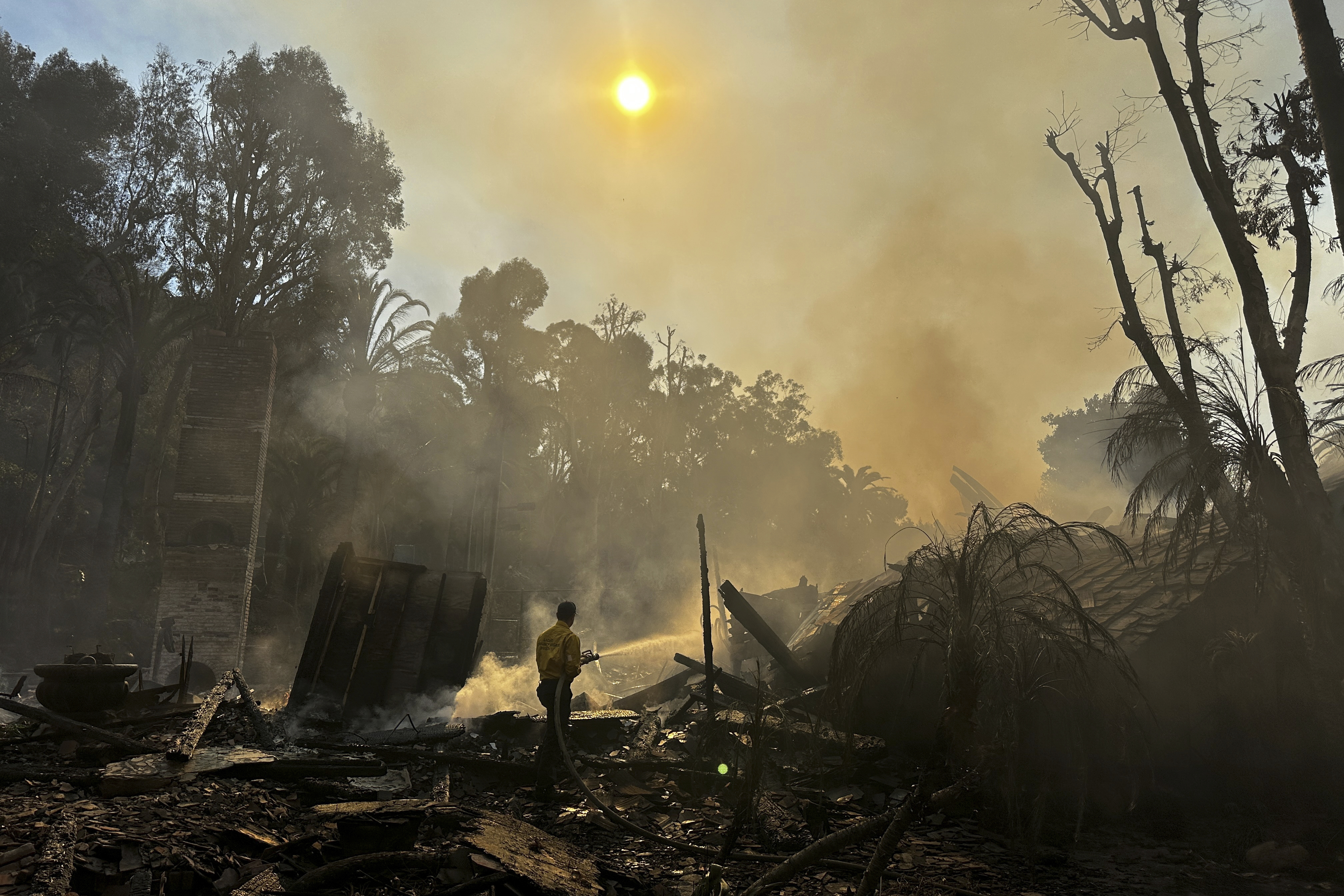 A firefighter hoses down hot spots around a fire-ravaged property after the Franklin Fire swept through Tuesday, Dec. 10, 2024, in Malibu, Calif. (AP Photo/Eugene Garcia)