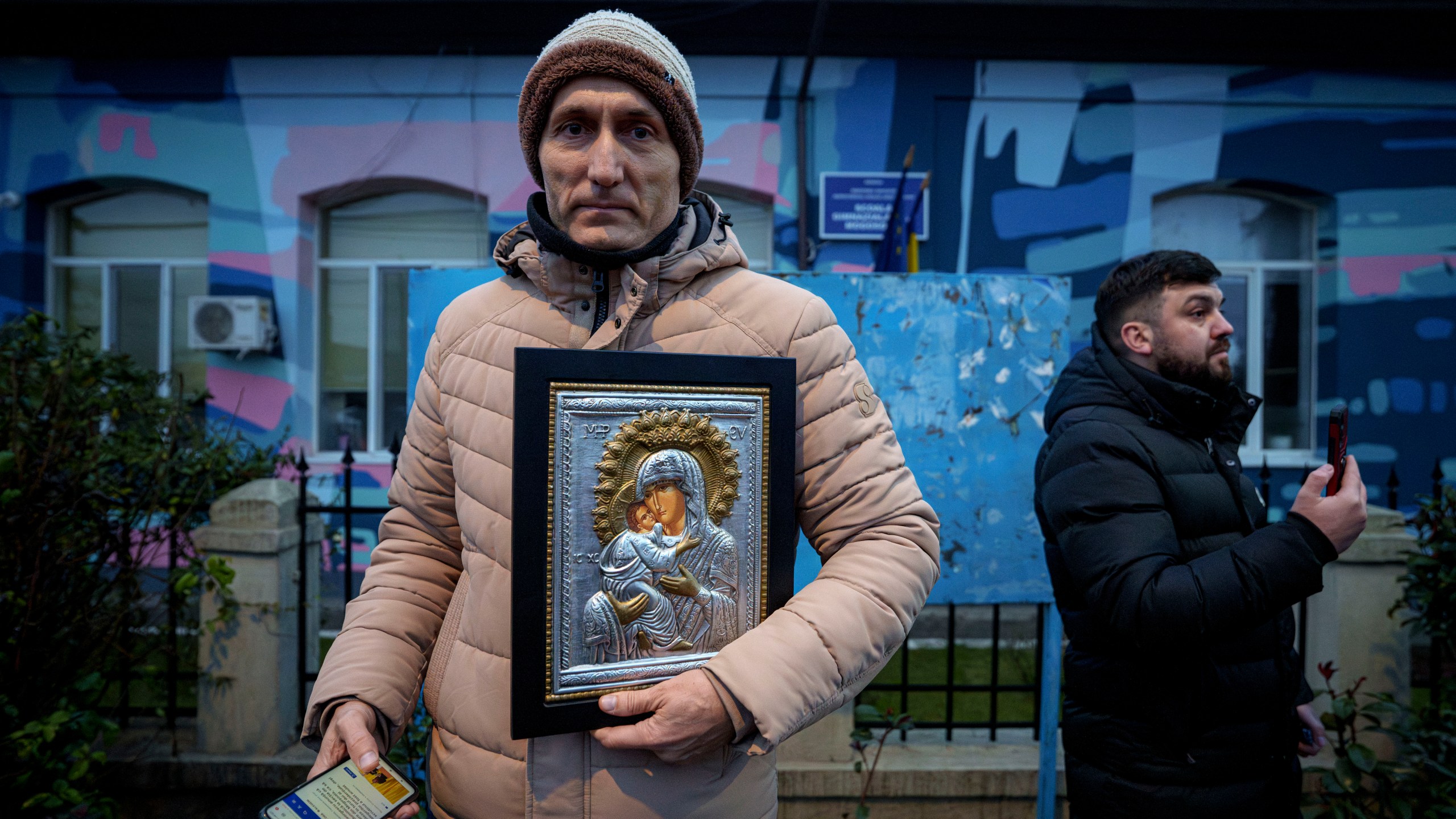 A man holds a religious icon outside the closed voting station where Calin Georgescu, an independent candidate for president who won the first round of presidential elections, was supposed to vote, after Romania's Constitutional Court annulled the first round of presidential elections, in Mogosoaia, Romania, Sunday, Dec. 8, 2024. (AP Photo/Andreea Alexandru)