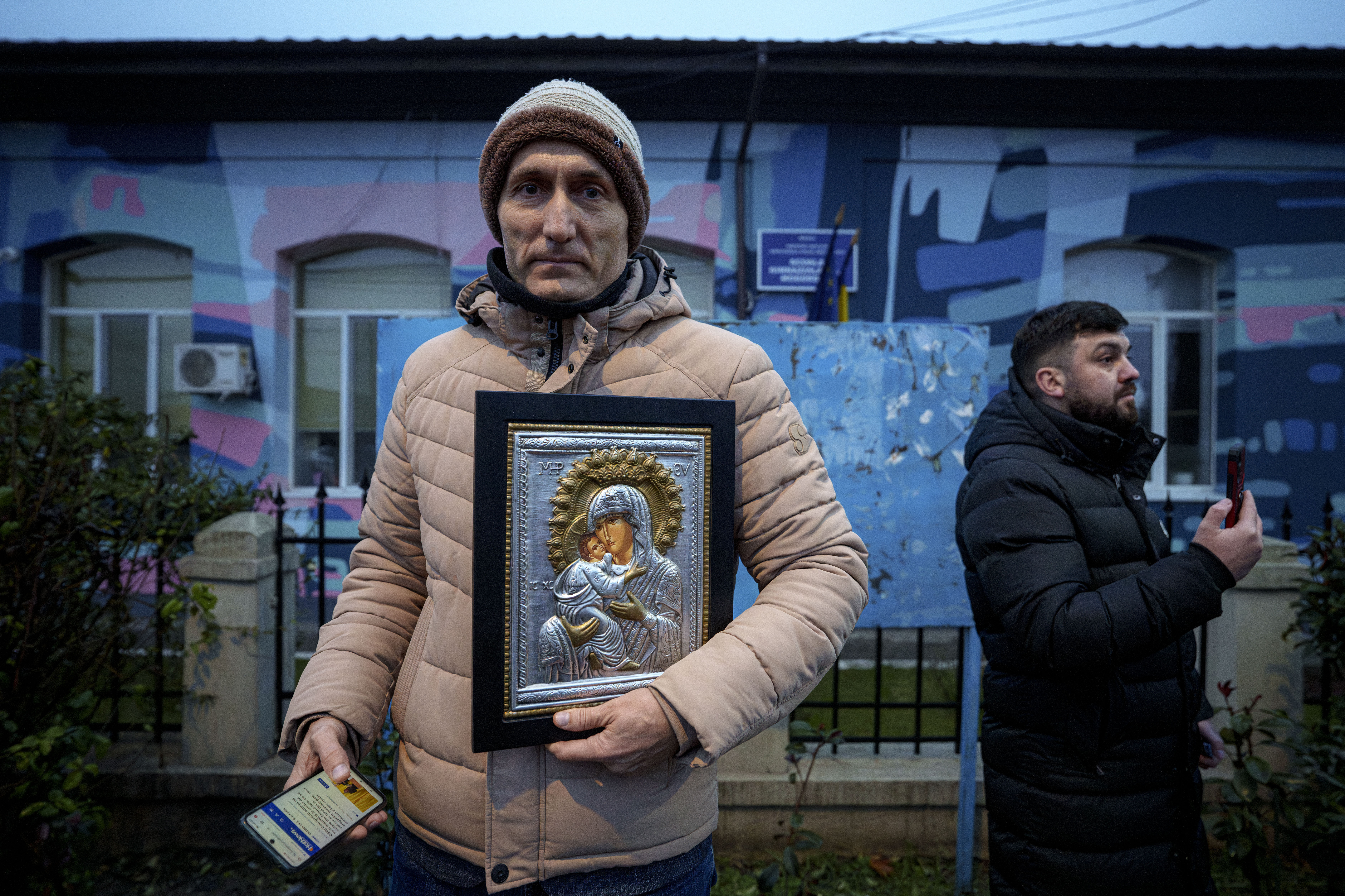 A man holds a religious icon outside the closed voting station where Calin Georgescu, an independent candidate for president who won the first round of presidential elections, was supposed to vote, after Romania's Constitutional Court annulled the first round of presidential elections, in Mogosoaia, Romania, Sunday, Dec. 8, 2024. (AP Photo/Andreea Alexandru)