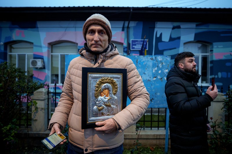 A man holds a religious icon outside the closed voting station where Calin Georgescu, an independent candidate for president who won the first round of presidential elections, was supposed to vote, after Romania's Constitutional Court annulled the first round of presidential elections, in Mogosoaia, Romania, Sunday, Dec. 8, 2024. (AP Photo/Andreea Alexandru)