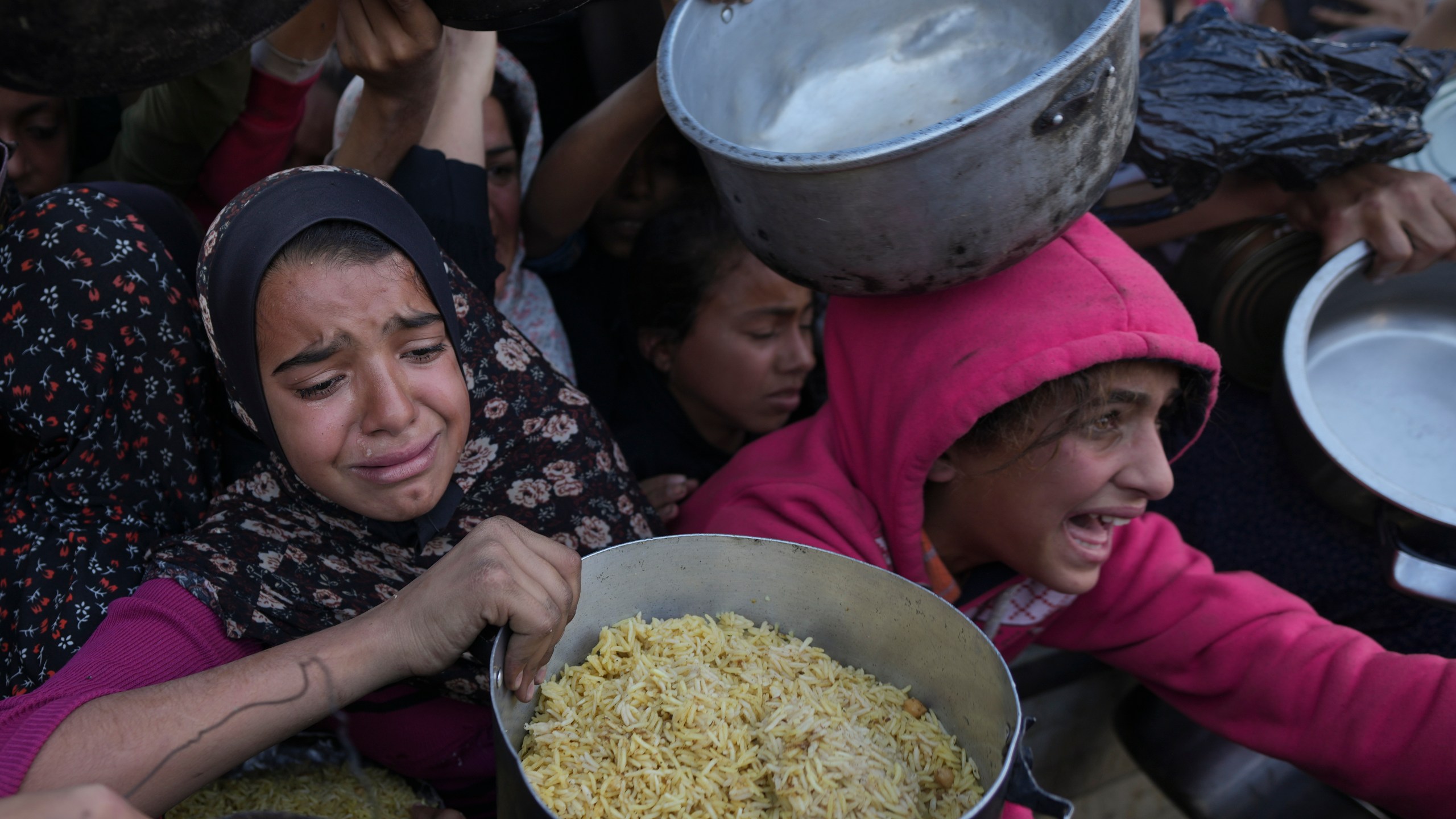 Palestinian girls struggle to reach for food at a distribution center in Khan Younis, Gaza Strip Friday, Dec. 6, 2024. (AP Photo/Abdel Kareem Hana)