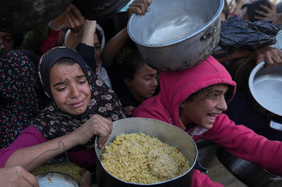 Palestinian girls struggle to reach for food at a distribution center in Khan Younis, Gaza Strip Friday, Dec. 6, 2024. (AP Photo/Abdel Kareem Hana)