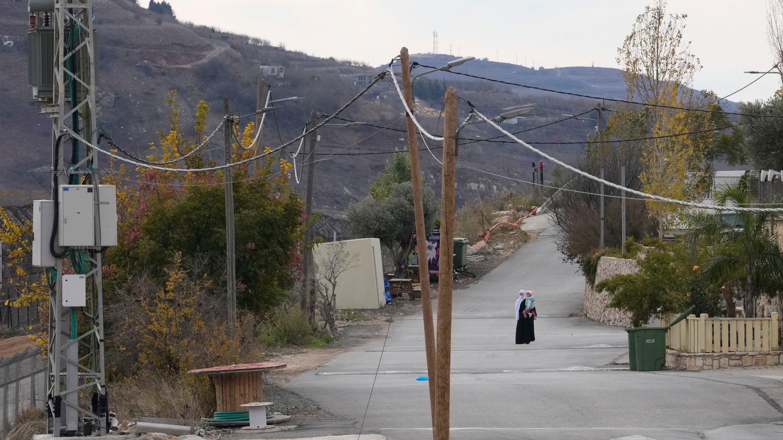 A woman holds her child near the so-called Alpha Line that separates the Israeli-annexed Golan Heights from Syria, in the town of Majdal Shams, Wednesday, Dec. 11, 2024. (AP Photo/Matias Delacroix)