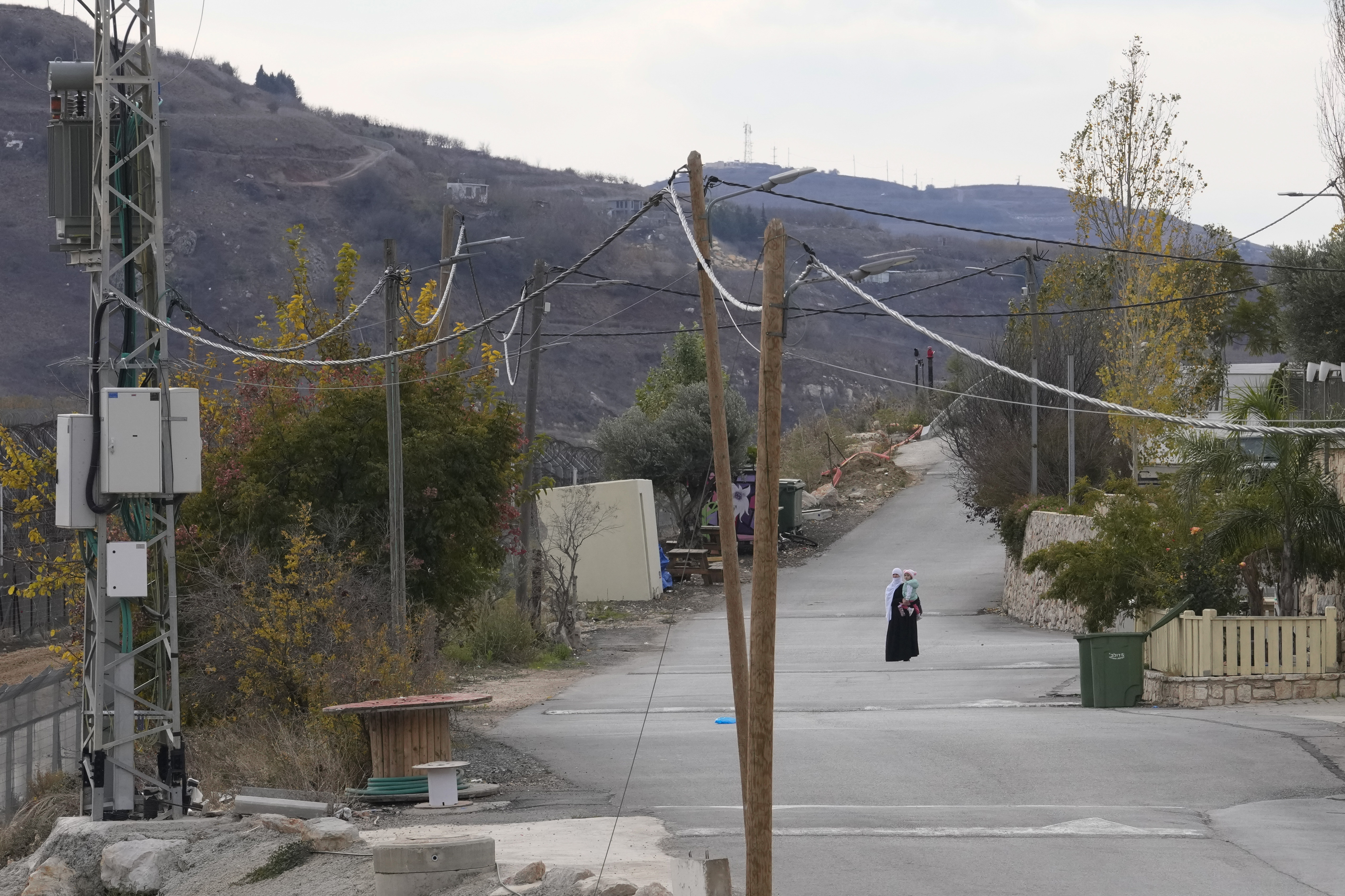 A woman holds her child near the so-called Alpha Line that separates the Israeli-annexed Golan Heights from Syria, in the town of Majdal Shams, Wednesday, Dec. 11, 2024. (AP Photo/Matias Delacroix)