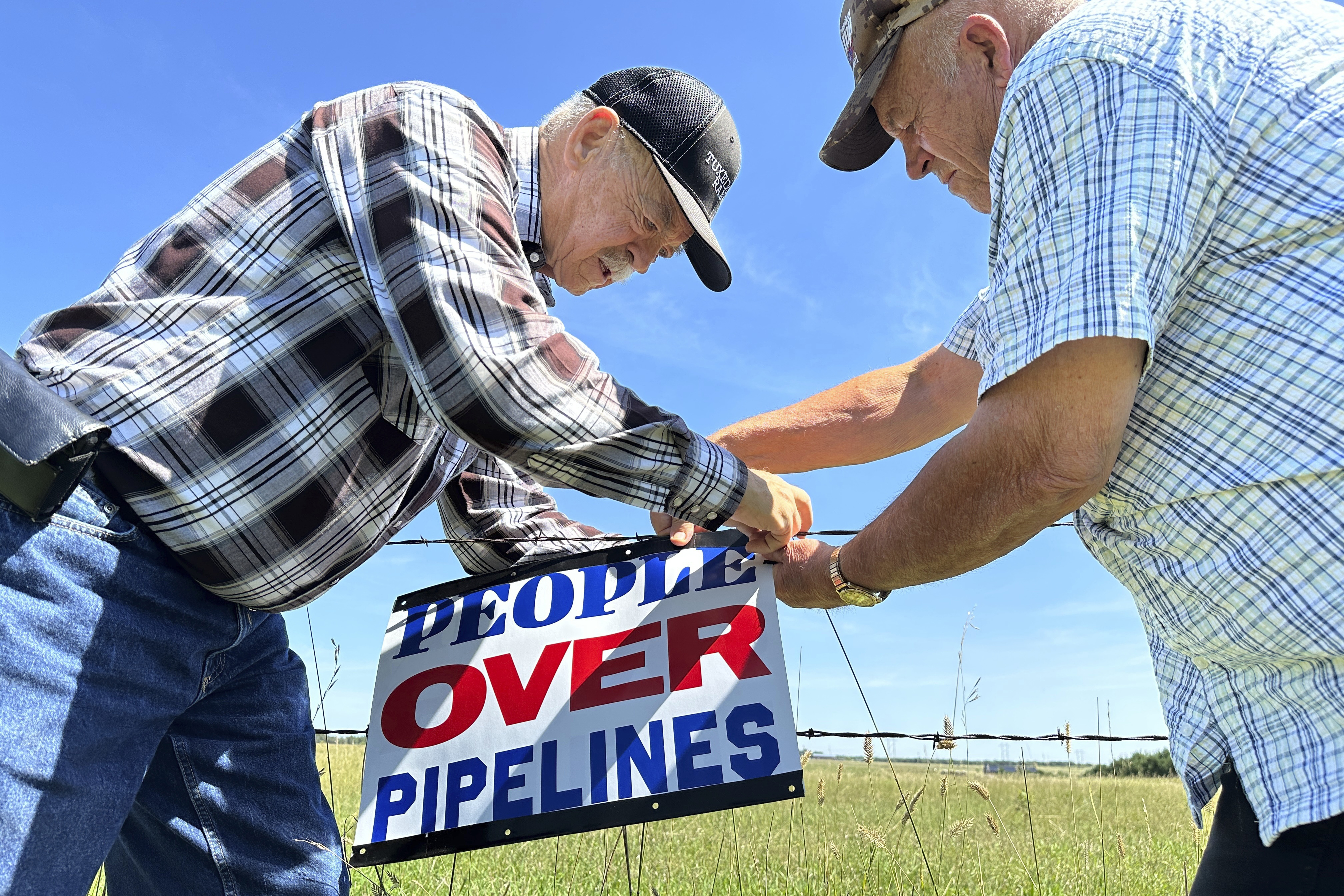 FILE - Gaylen Dewing, left, and Marvin Abraham affix a sign to a roadside fence east of Bismarck, N.D., Tuesday, Aug. 15, 2023, in opposition to Summit Carbon Solutions' proposed five-state, 2,000-mile pipeline network to carry carbon dioxide emissions from dozens of Midwestern ethanol plants to North Dakota for permanent storage deep underground. (AP Photo/Jack Dura, File)