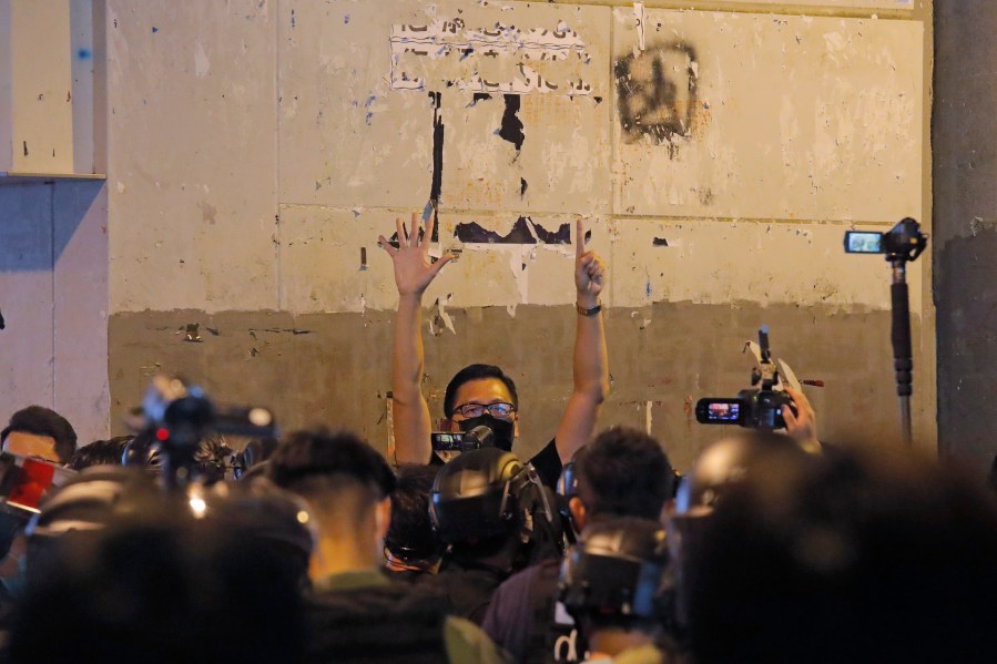 FILE- A pro-democracy lawmaker Lam Cheuk-ting, center, gestures with five fingers, signifying the "Five demands - not one less" as he is surrounded by riot police during a news conference to mark one-year anniversary of the Yuen Long subway attack at the subway station in Hong Kong, July 21, 2020. (AP Photo/Kin Cheung, File)