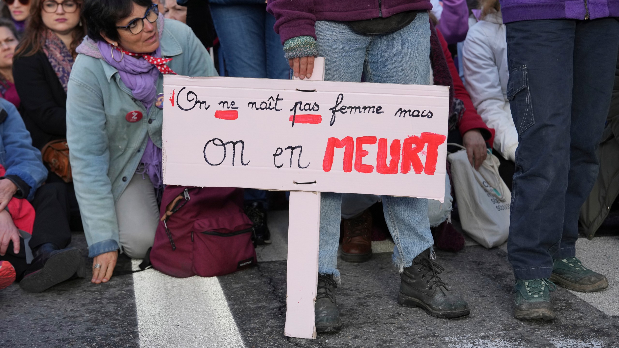 A woman sits by a placard reading " We are not born a woman but we die of it" during a women's rights demonstration, Saturday, Dec. 14, 2024 in Avignon, southern France, where the trial of dozens of men accused of raping Gisèle Pelicot while she was drugged and rendered unconscious by her husband is taking place. (AP Photo/Aurelien Morissard)