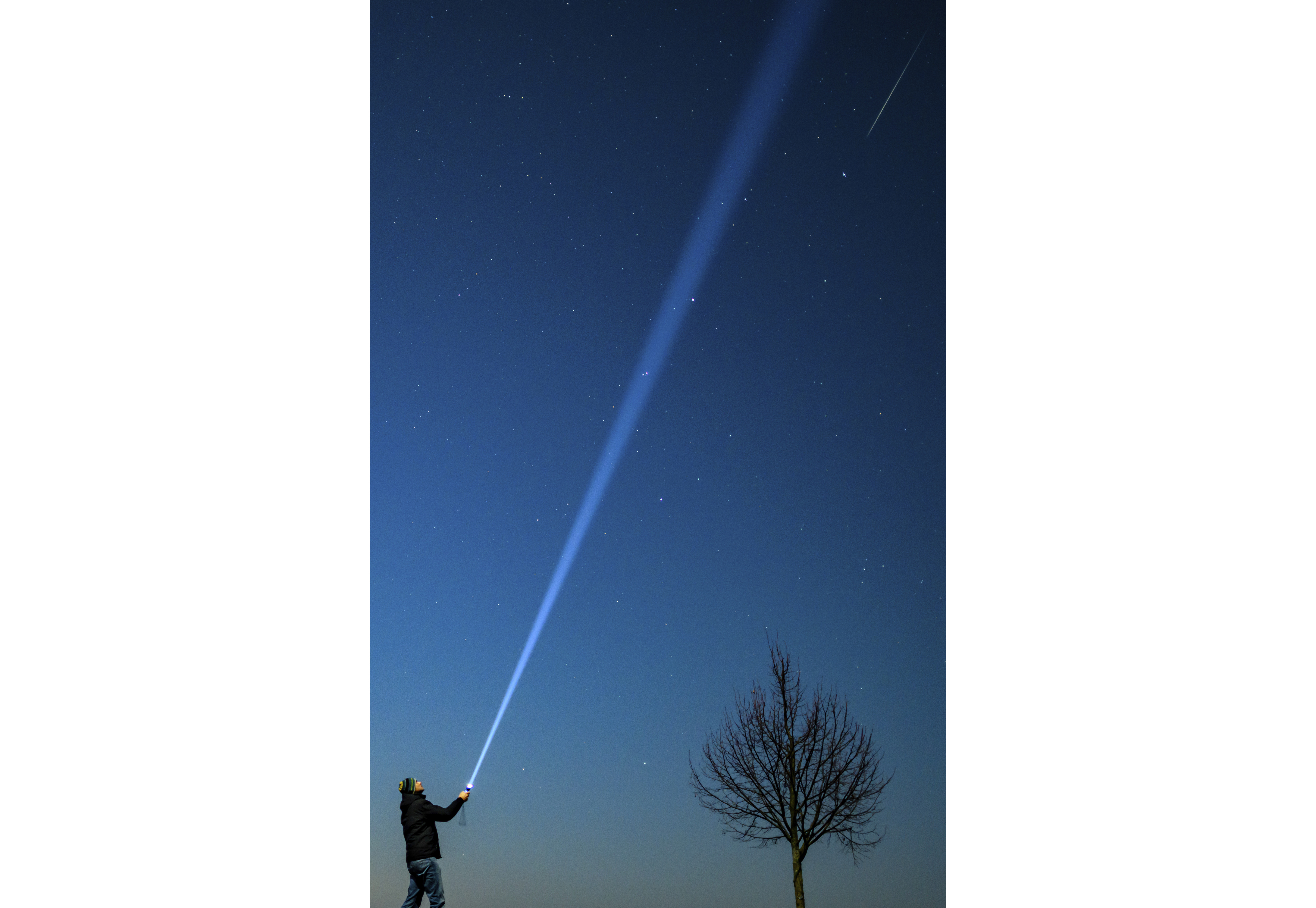 A shooting star, top right, is seen over eastern Brandenburg, Germany, while a person shines a flashlight into the night sky, Saturday, Dec. 14, 2024. (Patrick Pleul/dpa via AP)