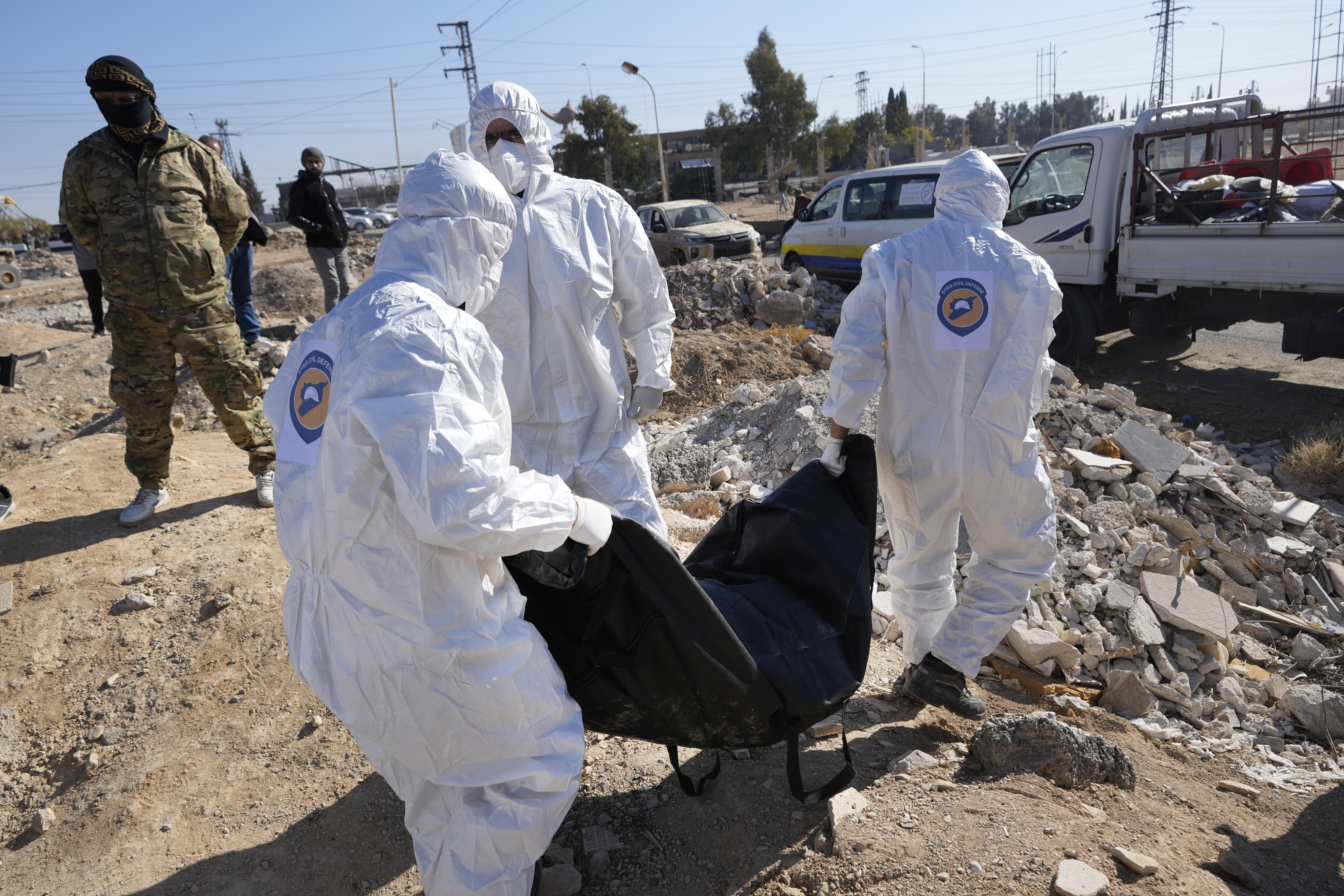 Syrian Civil Defense, known as the White Helmets, carry one of several bodies and human remains that were found dropped at an open field on a road that links to Damascus international airport, in Damascus, Syria, Monday, Dec. 16, 2024. (AP Photo/Hussein Malla)