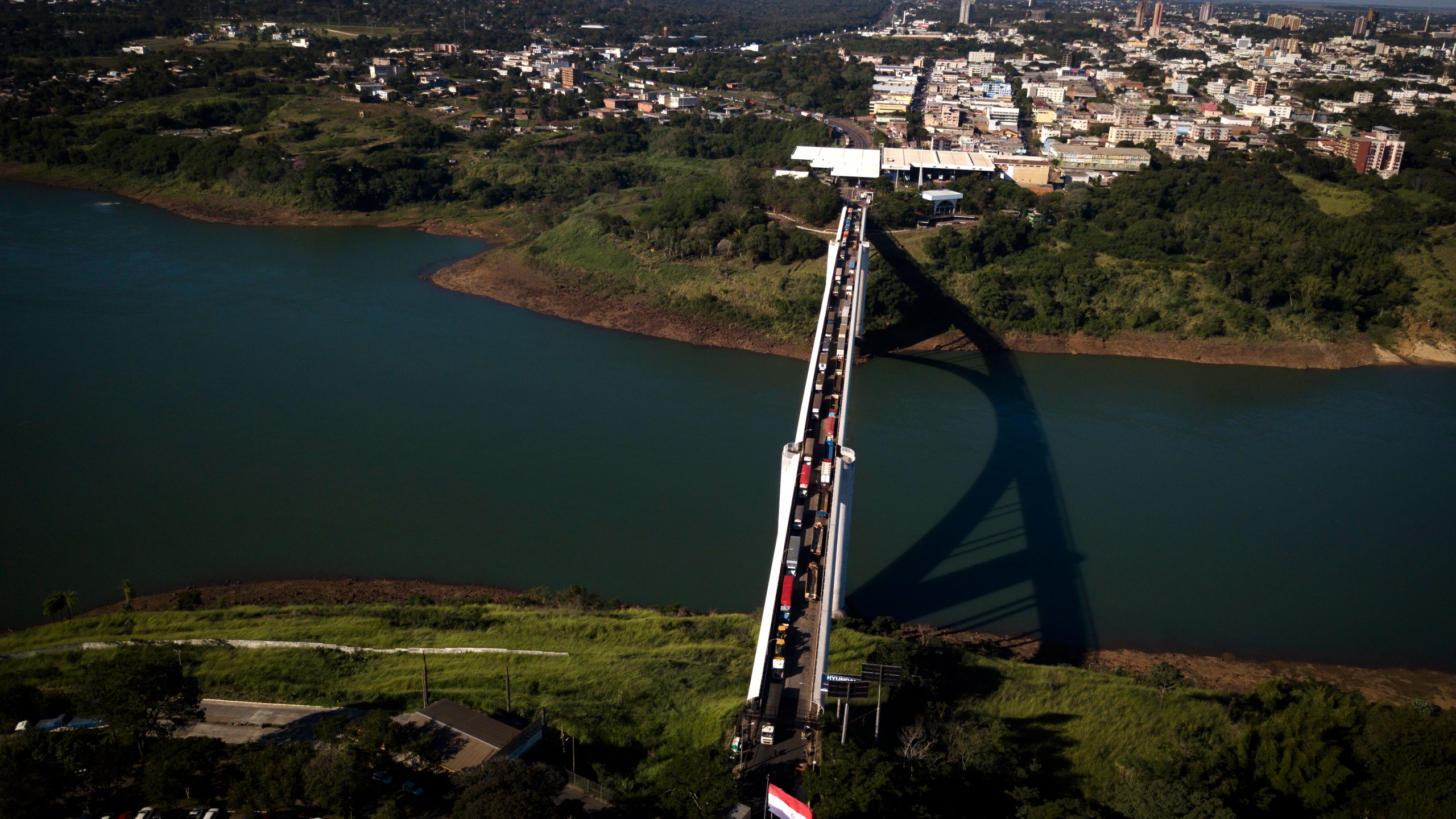 FILE - Trucks wait in line on Friendship Bridge over the Parana River, the border between Foz do Iguazu, Brazil, top, and Ciudad del Este, Paraguay, June 23, 2020. (AP Photo/Jorge Saenz, File)