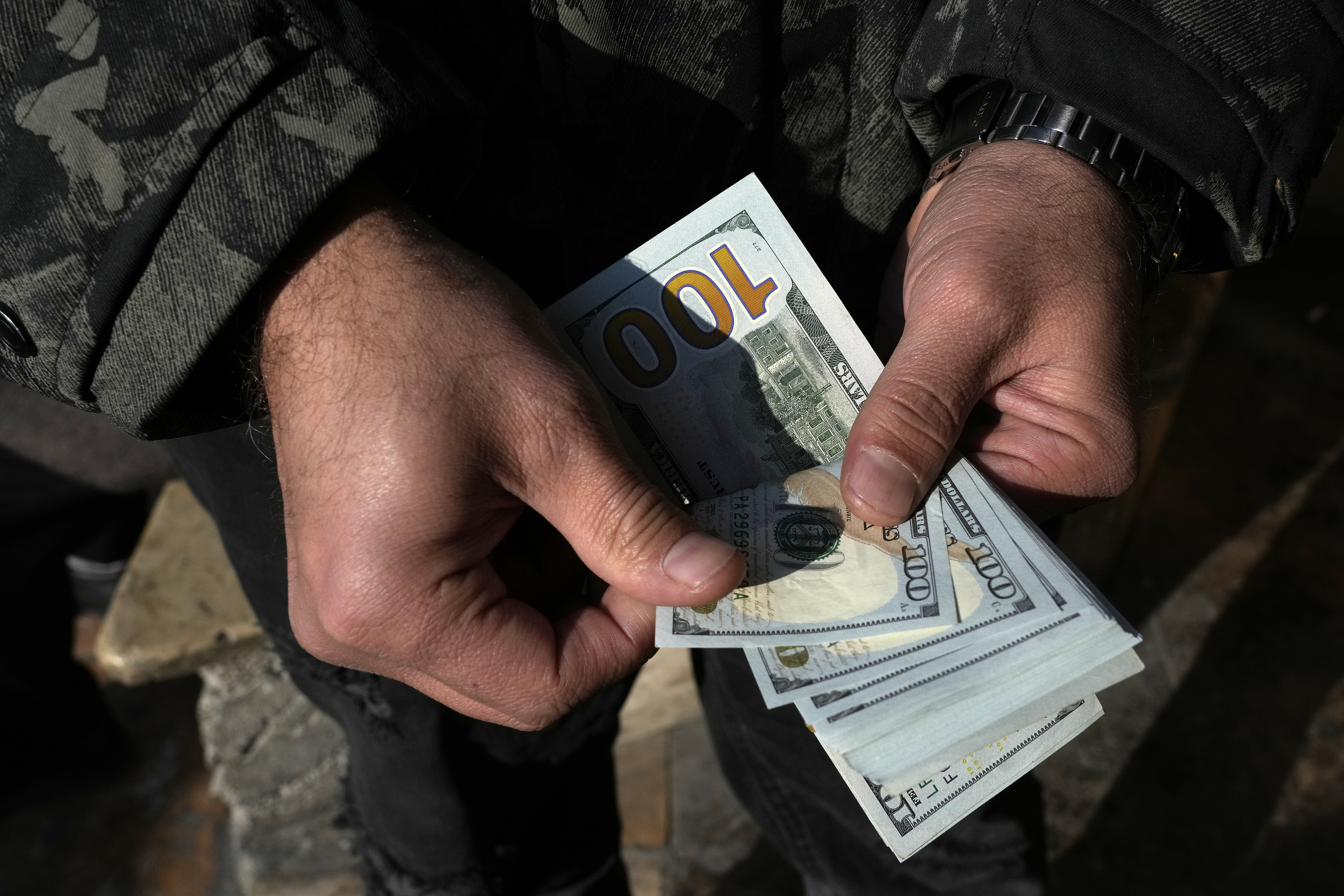 A man poses for a photo without showing his face as he counts U.S. dollars at Ferdowsi street, Tehran's go-to venue for foreign currency exchange, in downtown Tehran, Iran, Wednesday, Dec. 18, 2024. (AP Photo/Vahid Salemi)