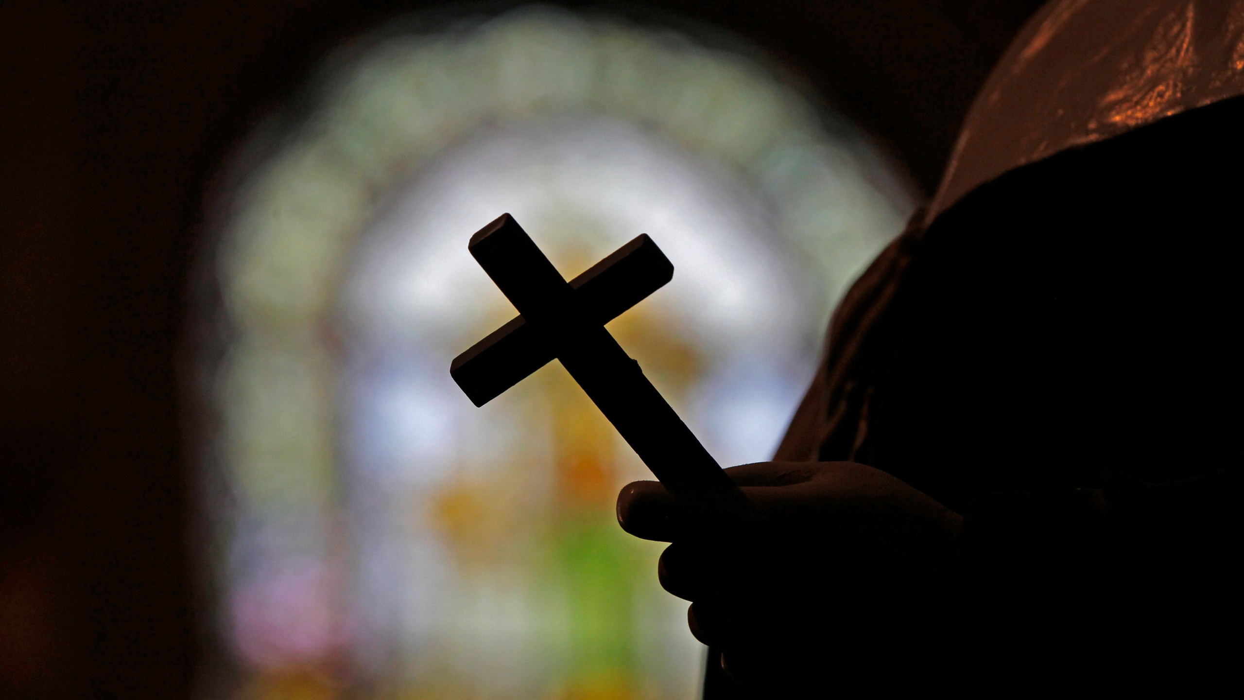 FILE - This Dec. 1, 2012 file photo shows a silhouette of a crucifix and a stained glass window inside a Catholic Church in New Orleans. (AP Photo/Gerald Herbert, File)