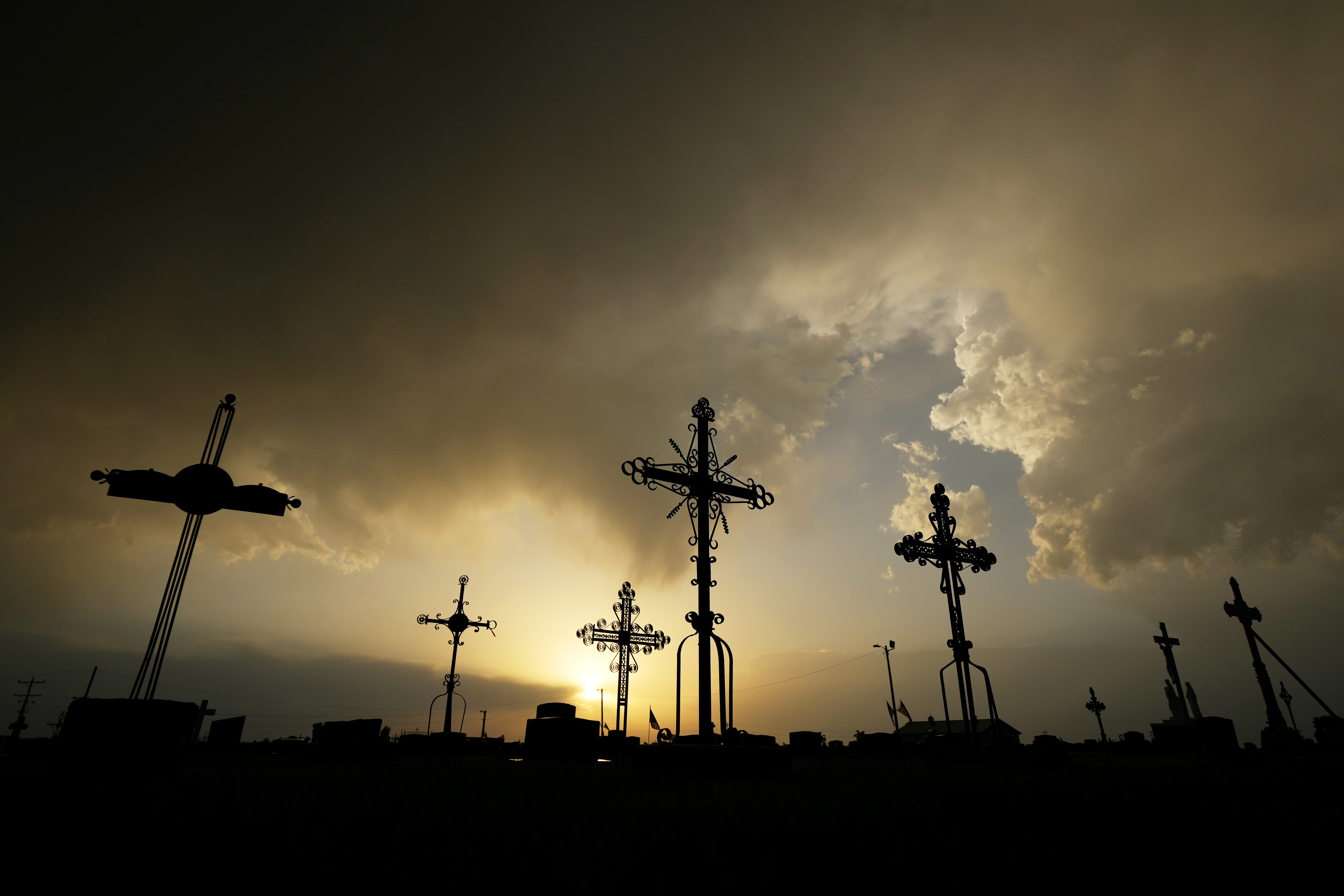 FILE - Iron crosses marking graves are silhouetted against storm clouds building over a cemetery Saturday, May 25, 2024, in Victoria, Kan. (AP Photo/Charlie Riedel, File)