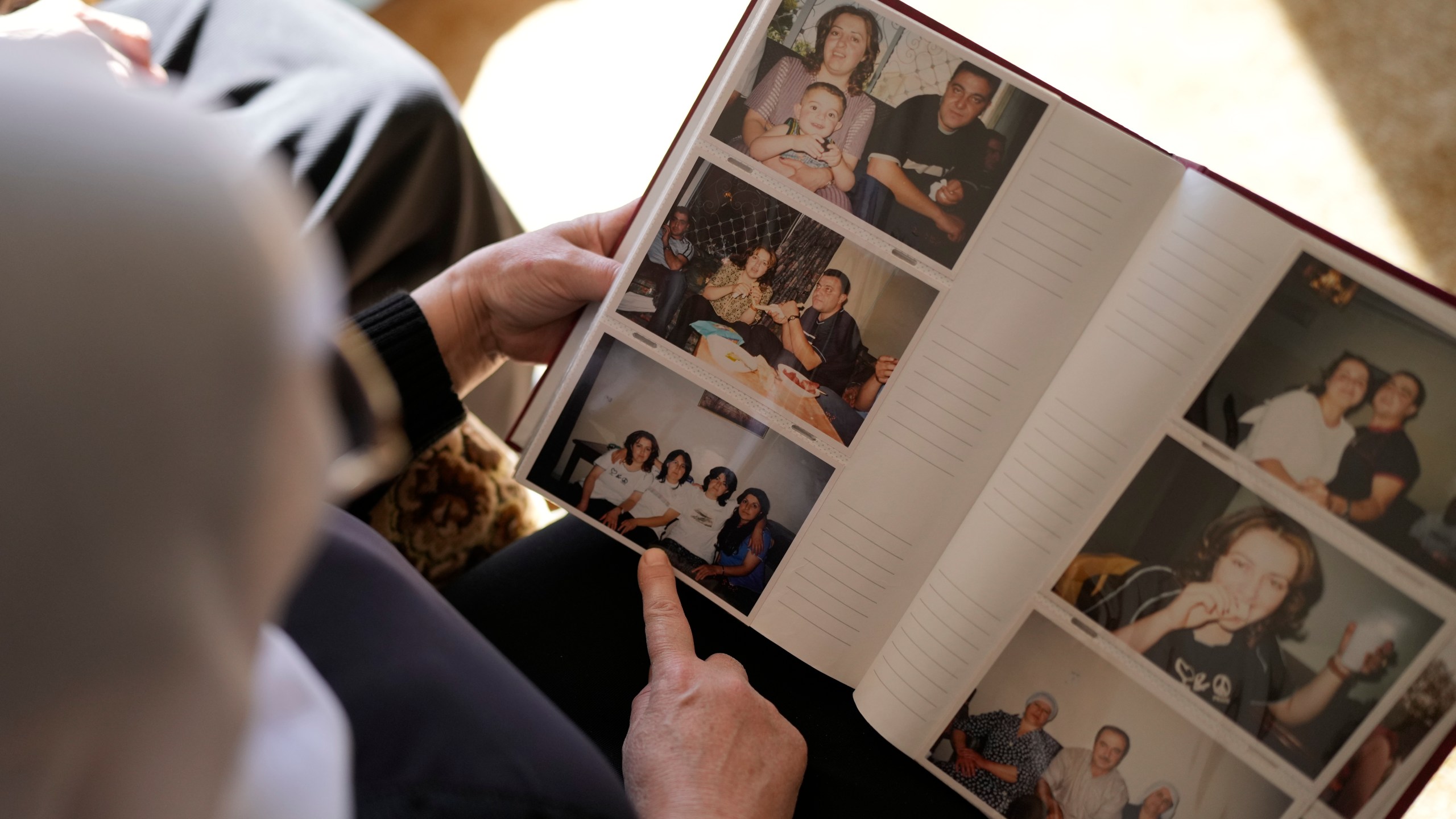 Samar Safadi looks at family photos after speaking by phone with her sister, Sawsan, who is inside the buffer zone near the "Alpha Line" that separates the Israeli-controlled Golan Heights from Syria, in the town of Majdal Shams, Wednesday, Dec. 18, 2024. (AP Photo/Matias Delacroix)