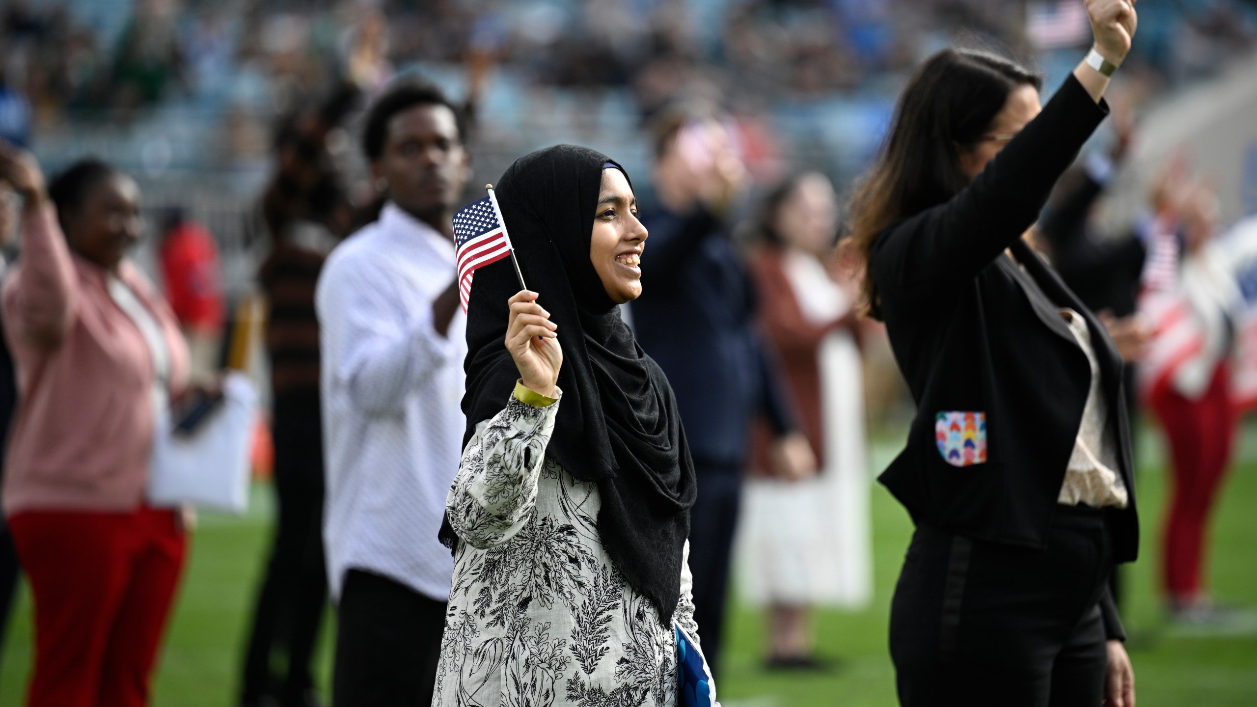 FILE - New United States citizens wave American flags during a naturalization ceremony during halftime at an NFL football game between the Jacksonville Jaguars and the New York Jets, Dec. 15, 2024, in Jacksonville, Fla. (AP Photo/Phelan M. Ebenhack, File)