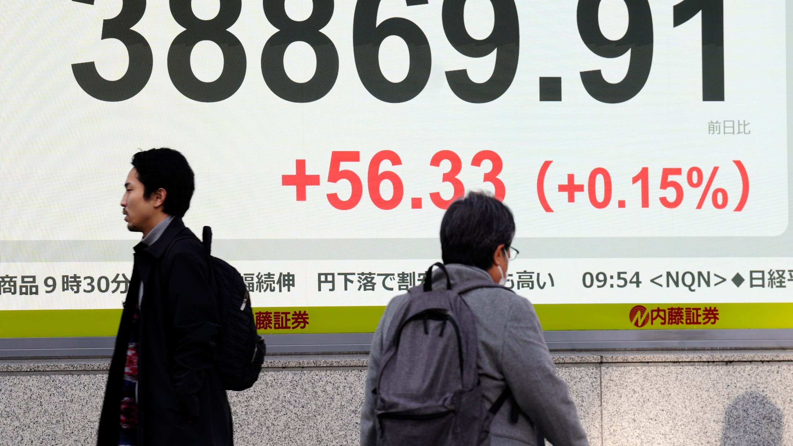 People walk in front of an electronic stock board showing Japan's Nikkei index at a securities firm Friday, Dec. 20, 2024, in Tokyo. (AP Photo/Eugene Hoshiko)