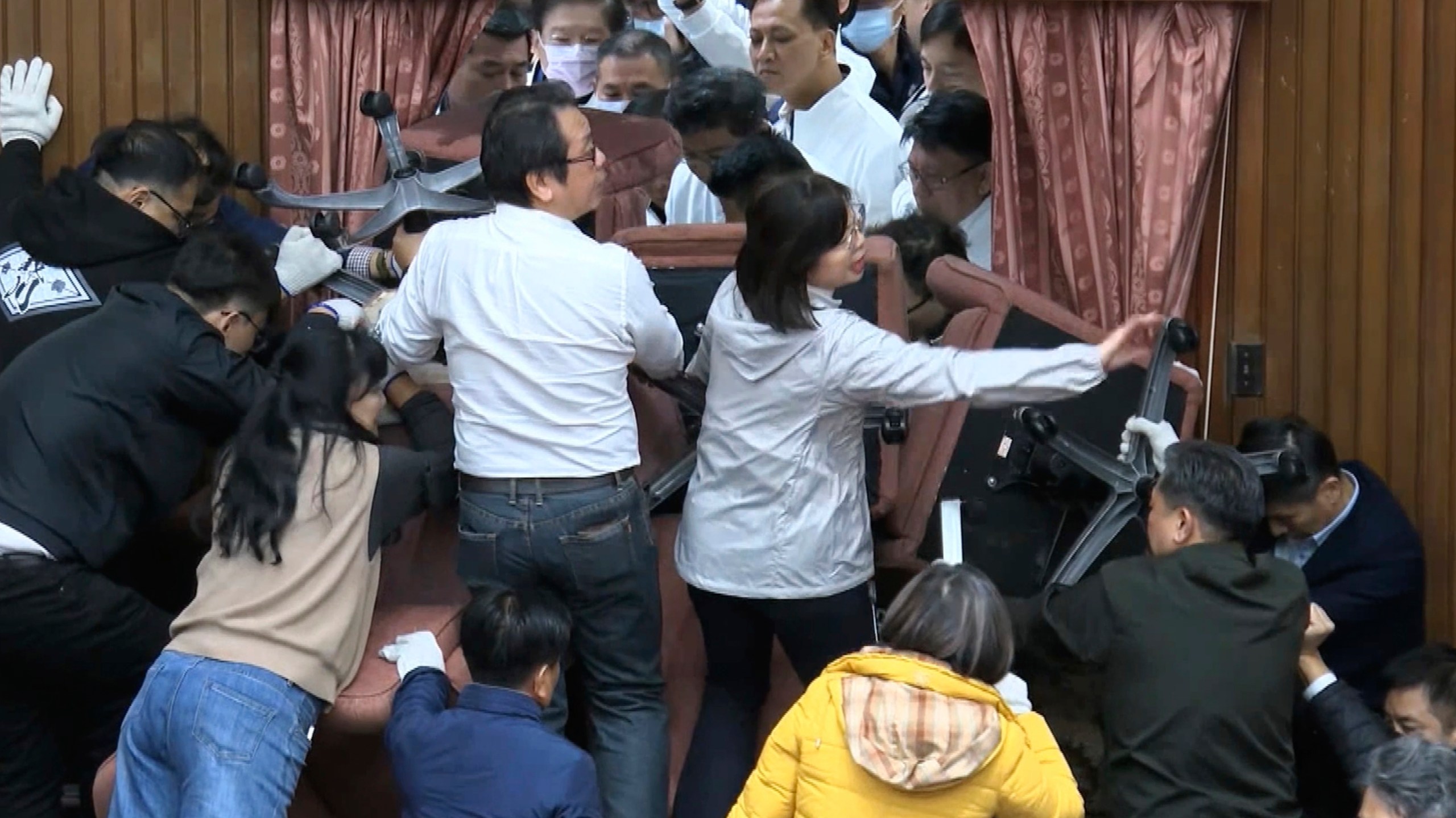 In this image made from video by Taiwan's EBC, lawmakers from the Democratic Progressive Party use chairs to block the entrance as members of the Nationalist Party, or Kuomintang try to break into the Legislature in Taipei, Taiwan on Friday, Dec. 20, 2024. (EBC via AP)