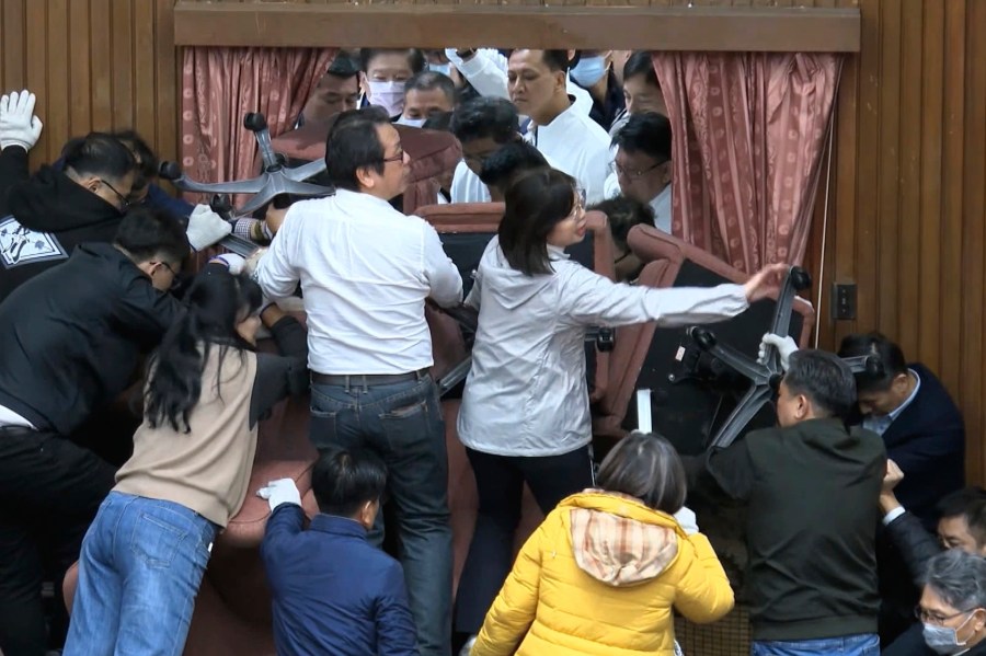 In this image made from video by Taiwan's EBC, lawmakers from the Democratic Progressive Party use chairs to block the entrance as members of the Nationalist Party, or Kuomintang try to break into the Legislature in Taipei, Taiwan on Friday, Dec. 20, 2024. (EBC via AP)