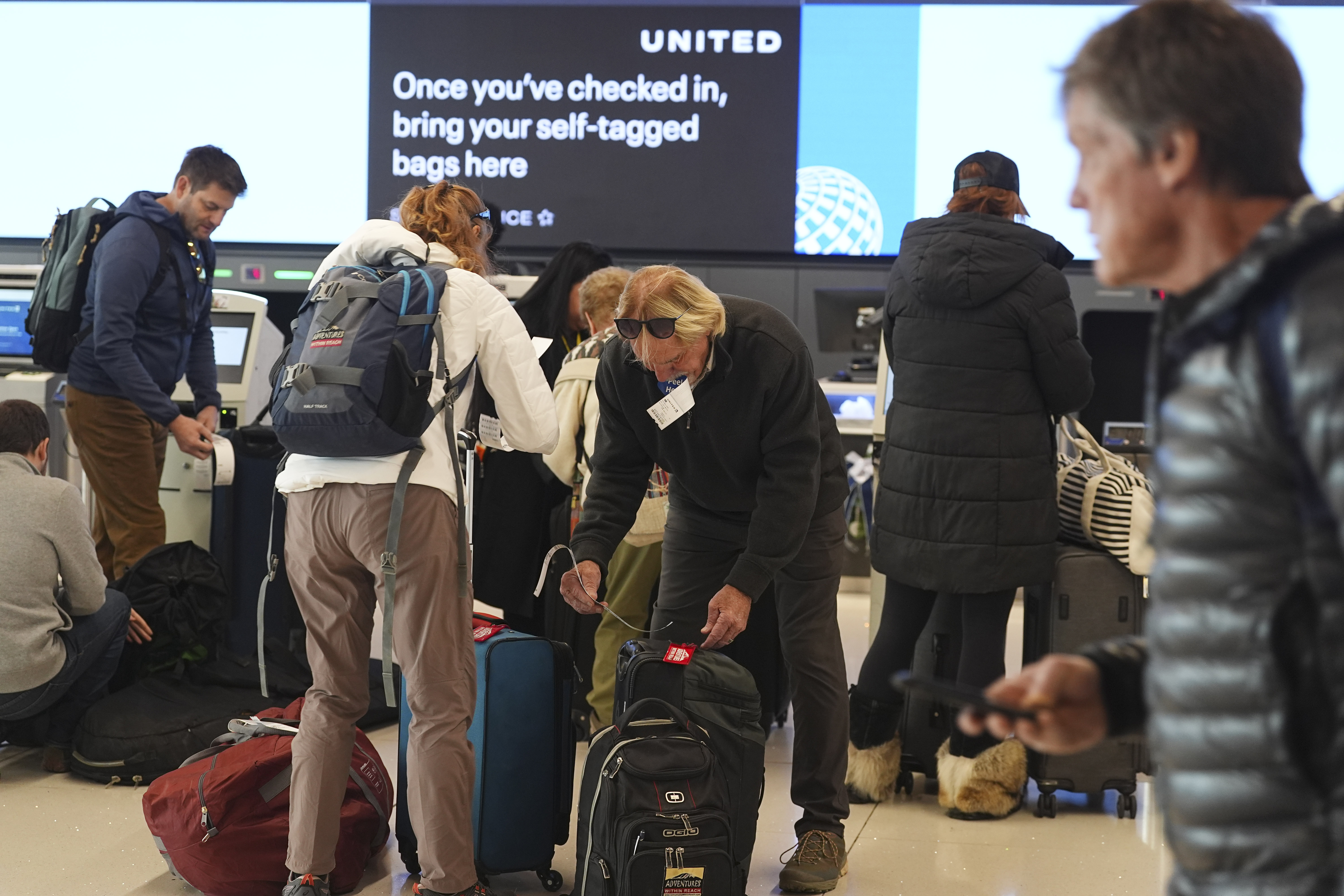 Travelers attach tags to their bags after checking in at the United Airlines counter at Denver International Airport, Saturday, Dec. 14, 2024, in Denver. (AP Photo/David Zalubowski)